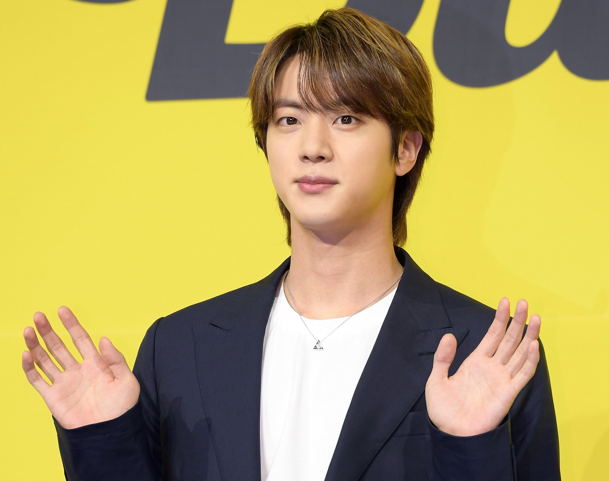 Jin of BTS holds up both hands while stanidng in front of a yellow background at BTS' 'Butter' press conference