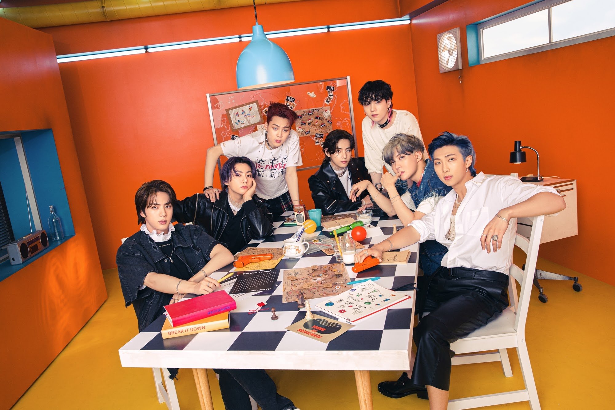 Jin, Jungkook, Jimin, V, Suga, J-Hope, and RM of BTS pose around a black-and-white table