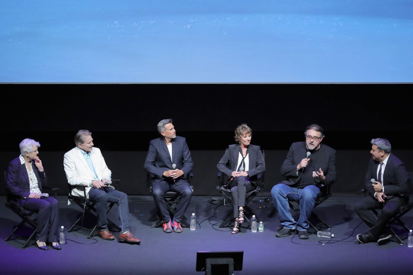 Six people that are from the cast of Disney's 'Beauty and the Beast' sitting in front a black background dressed professionally.