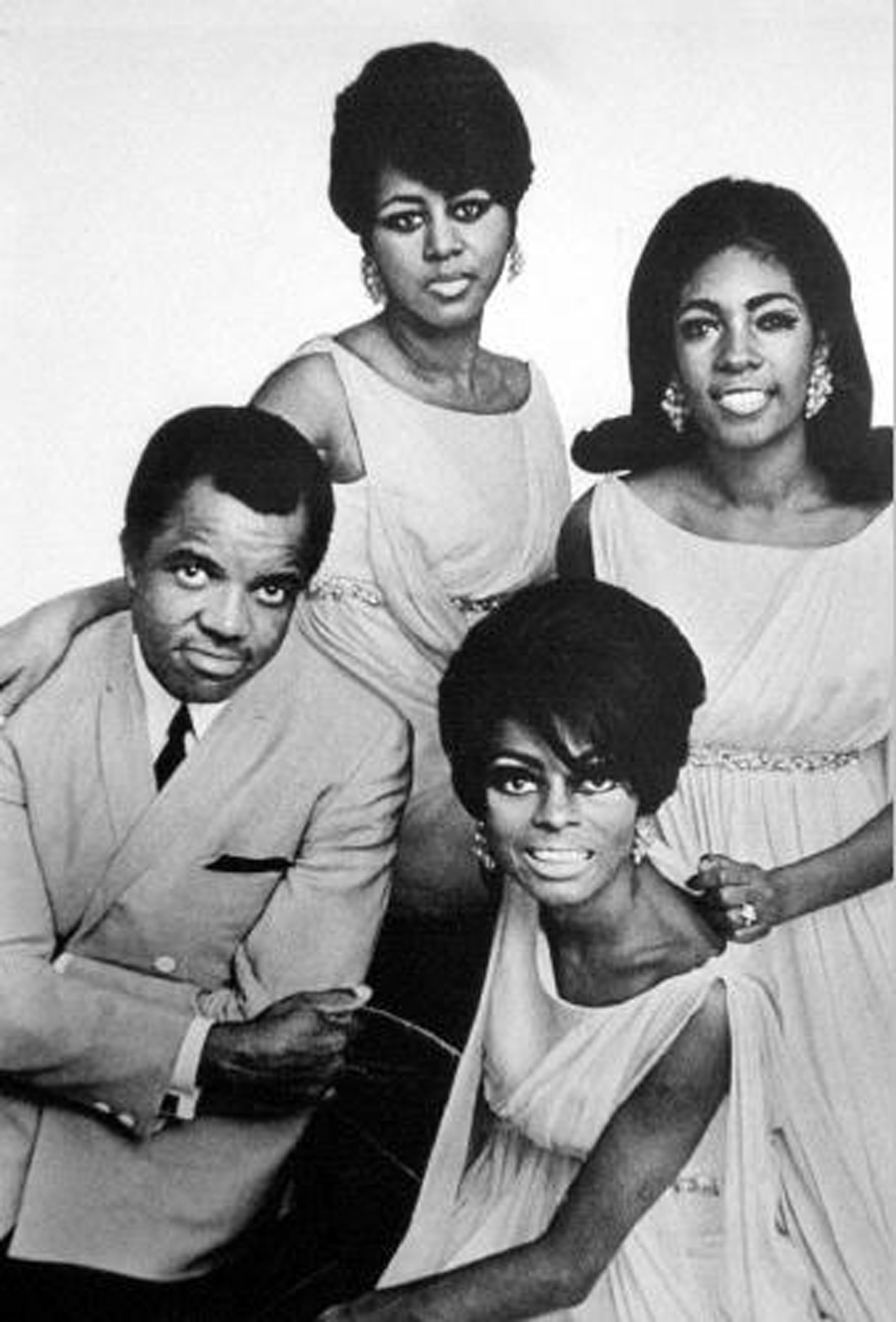 Berry Gordy with Diana Ross and The Supremes smiling for the camera in a black and white photo.