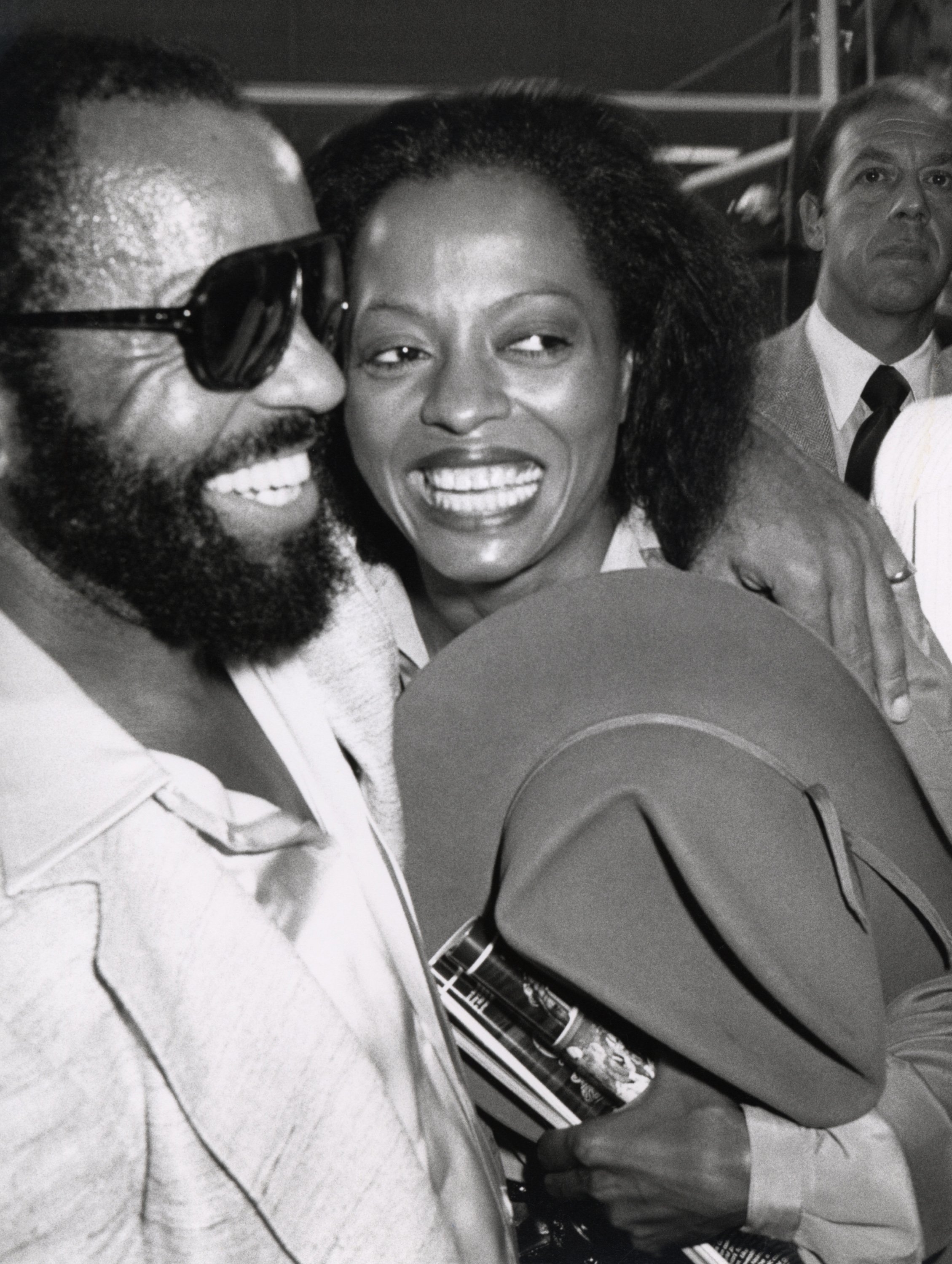 Berry Gordy and Diana Ross smiling and hugging each other while attending a boxing event.