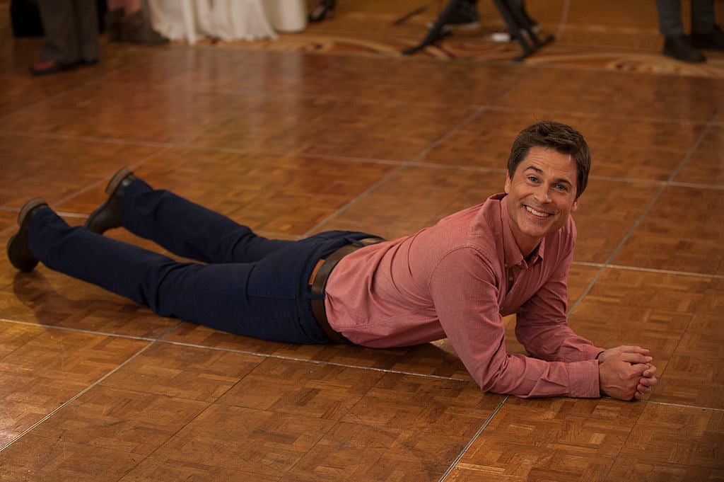 Rob Lowe as Chris Traeger is propped up on his elbows as he lays on a hardwood dance floor. 