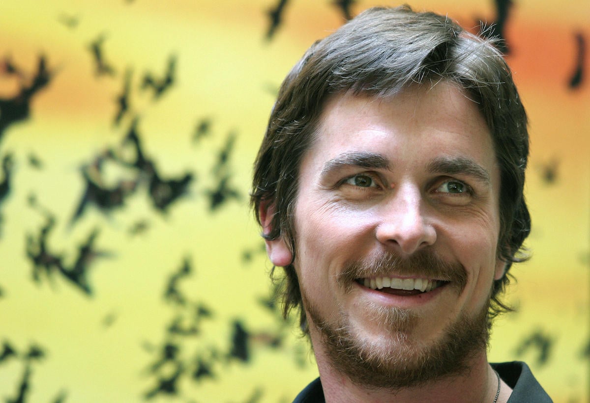Christian Bale poses for photographers in front of a bat-filled background