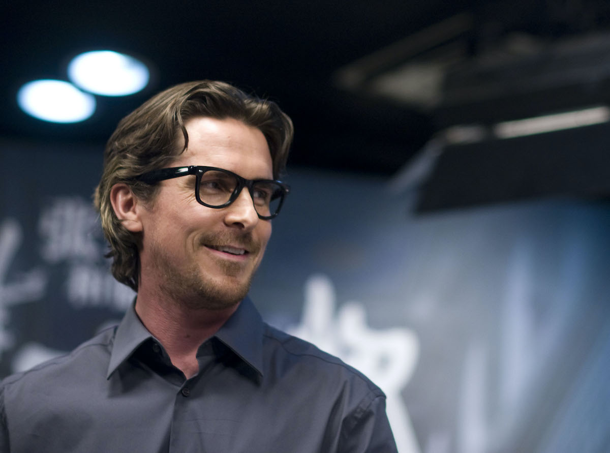 Christian Bale wears glasses and smiles at a press conference