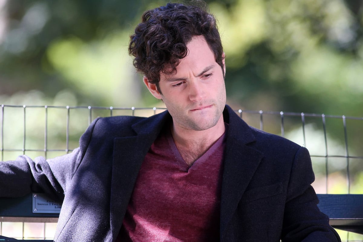 Penn Badgley as Dan Humphrey bites his lip as he sits on a park bench in 'Gossip Girl'