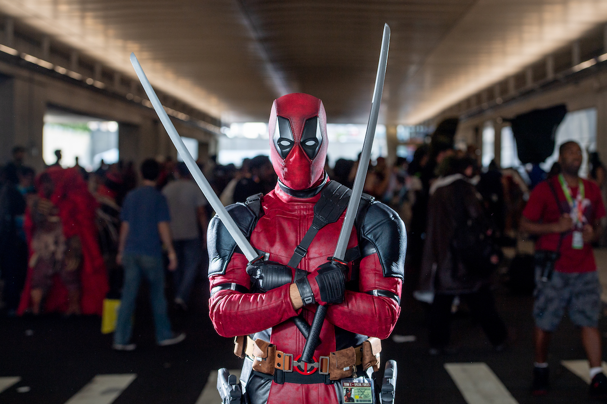A fan cosplays as Deadpool in full costume while holding swords