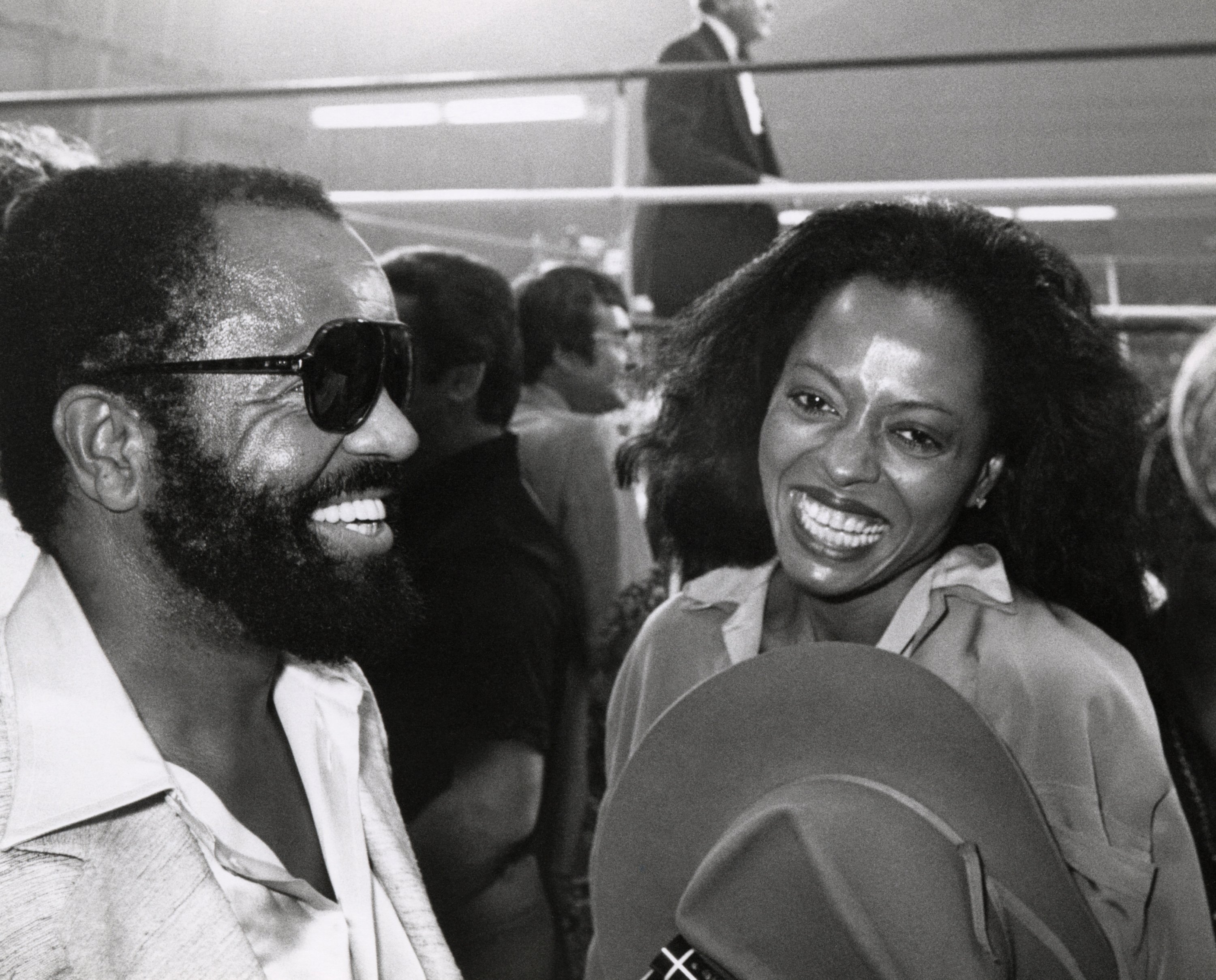 A black and white photo of Diana Ross and Berry Gordy smiling at a boxing match.
