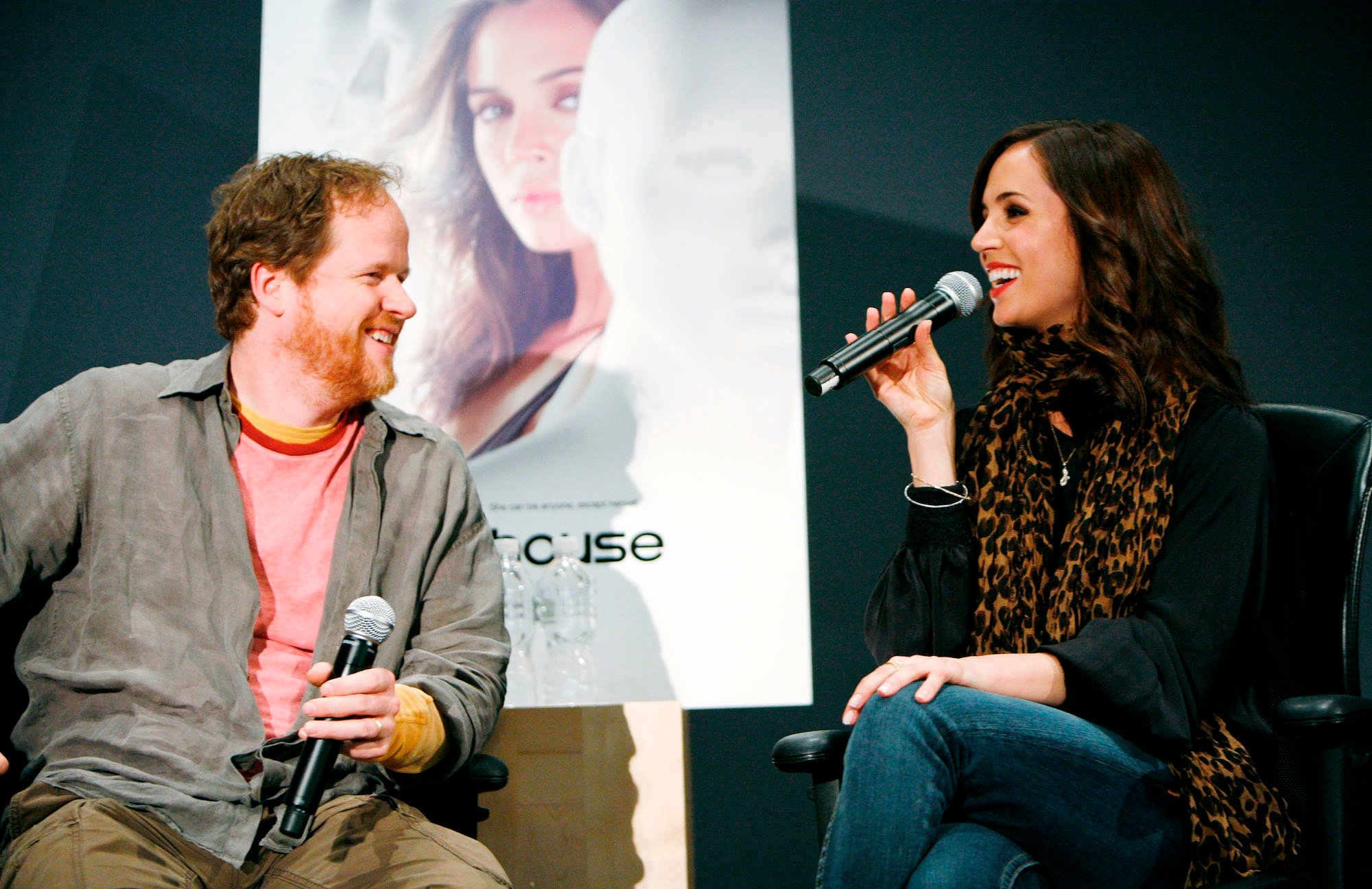 Joss Whedon and Eliza Dushku smiling, talking into microphones