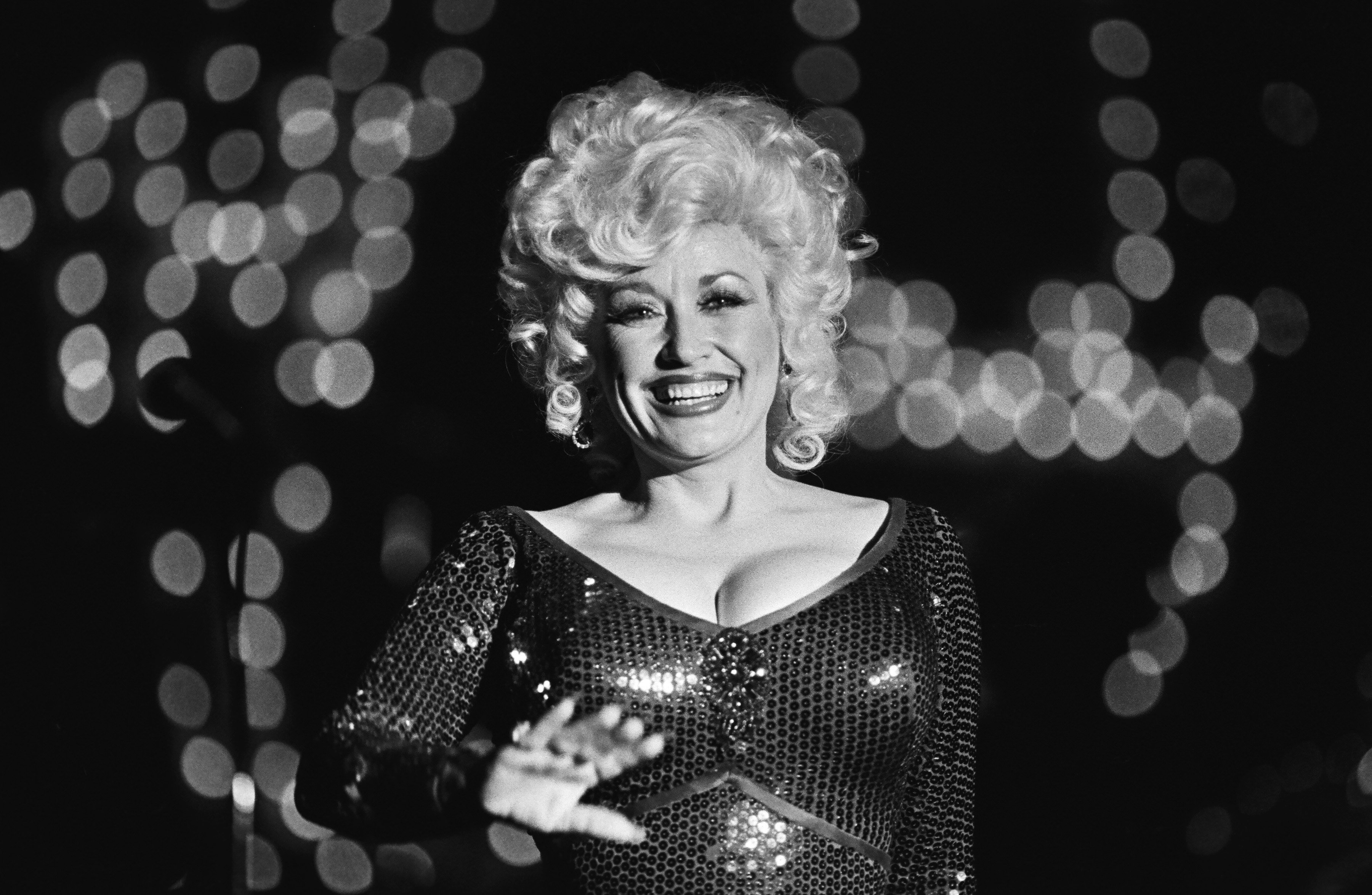 Dolly Parton performs at Harrah's Club in 1980. She's photographed in black and white, waving to the camera.