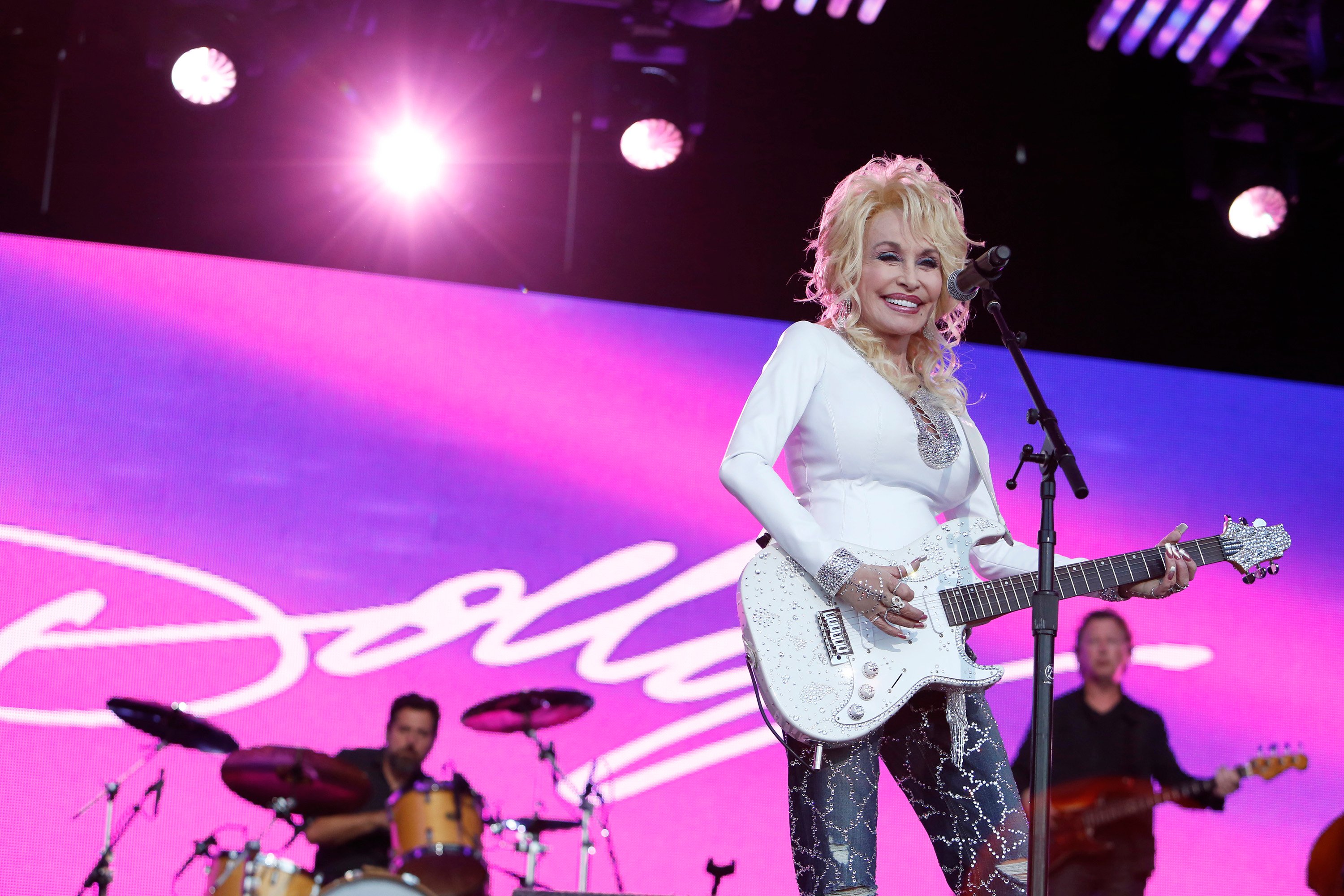 Dolly Parton performing on the 'Jimmy Kimmel Live' stage. She's wearing a white top and playing a white guitar.