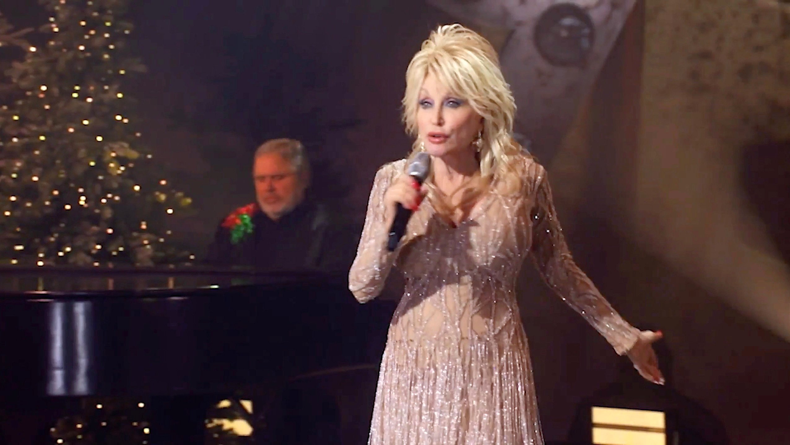 Dolly Parton performs for Billboard's Women in Music. She's in a pale pink dress and singing into a microphone.