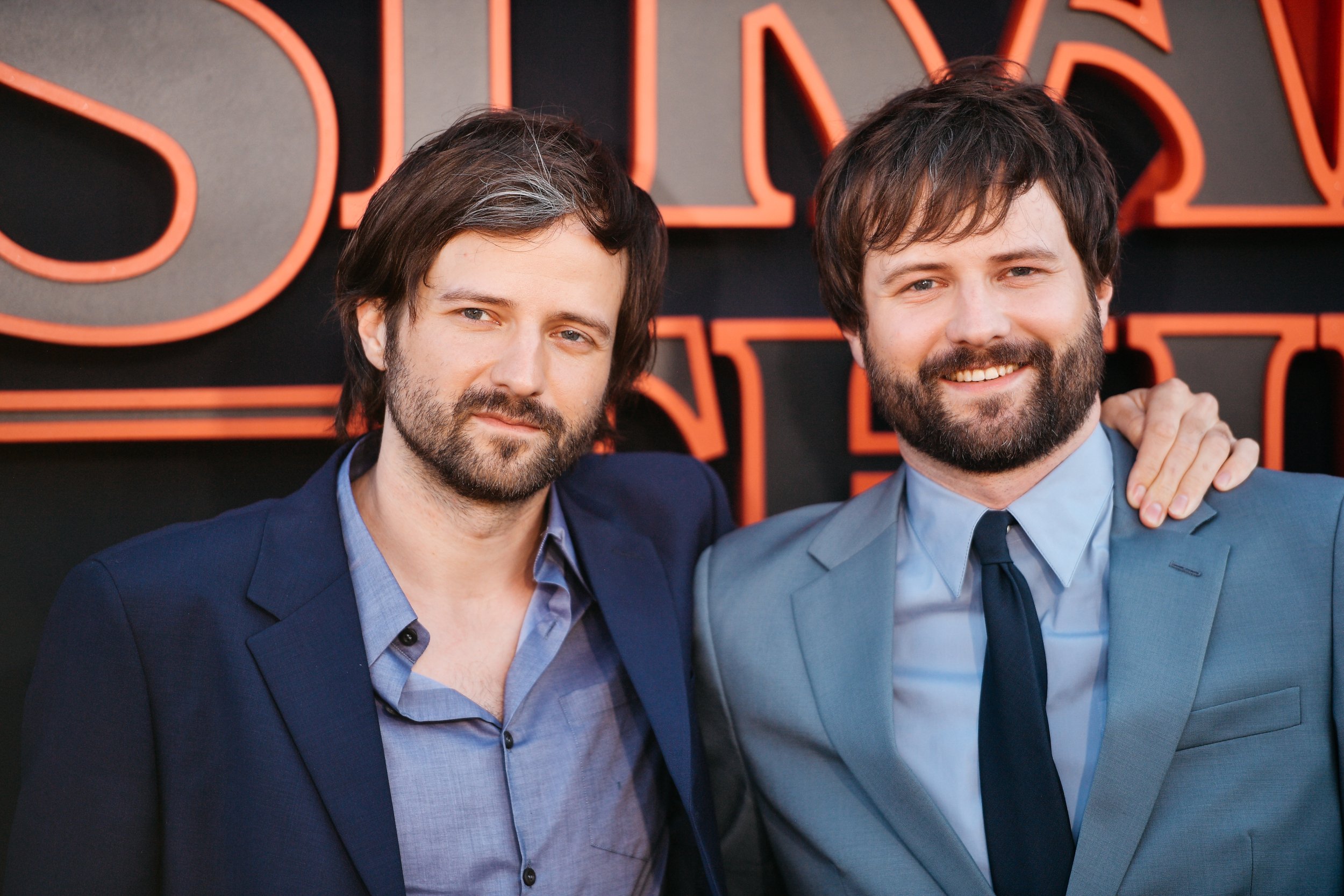 'Stranger Things' creators Matt and Ross Duffer stand in suits in front of a Netflix wall