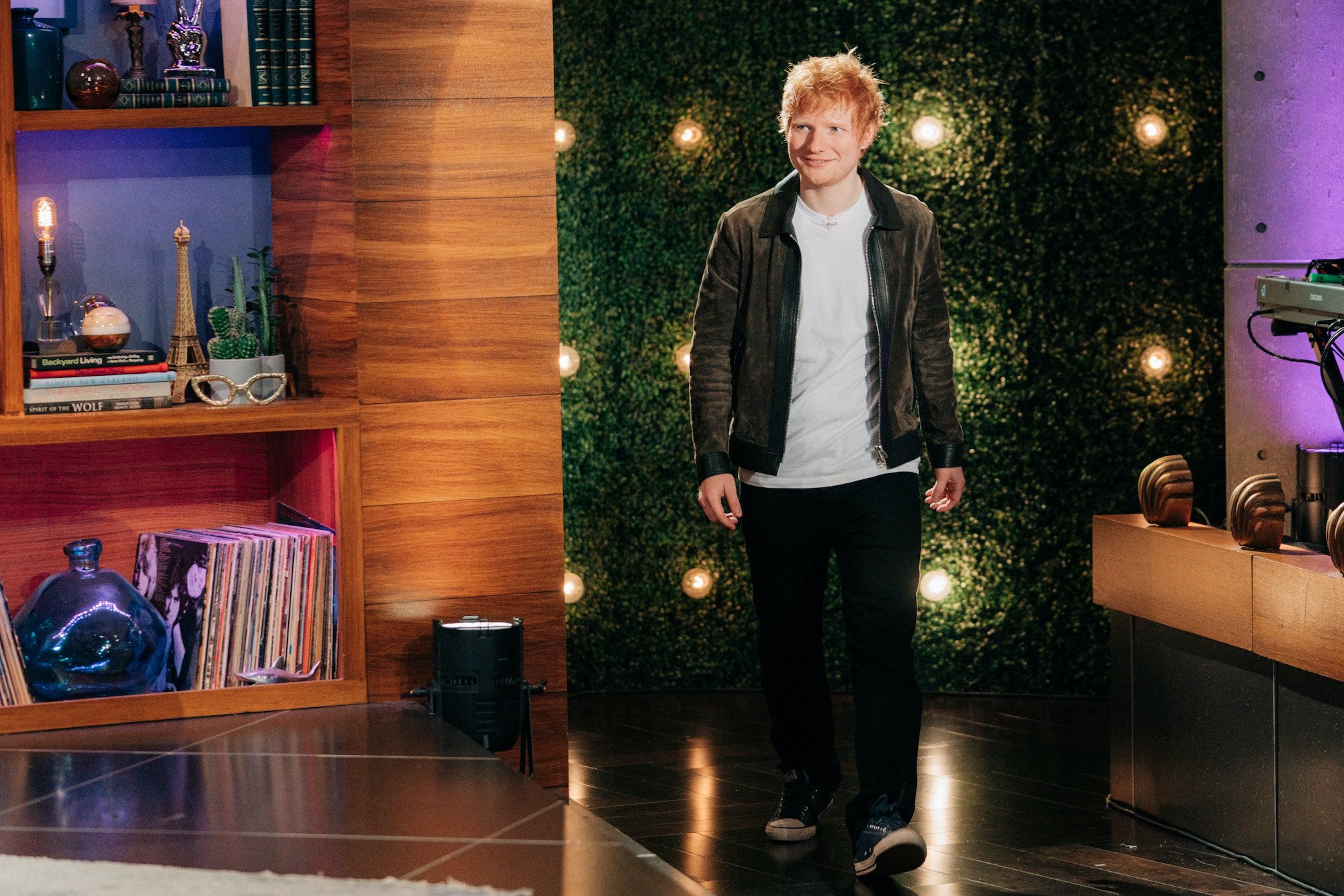 Ed Sheeran smiling, walking in front of a green background