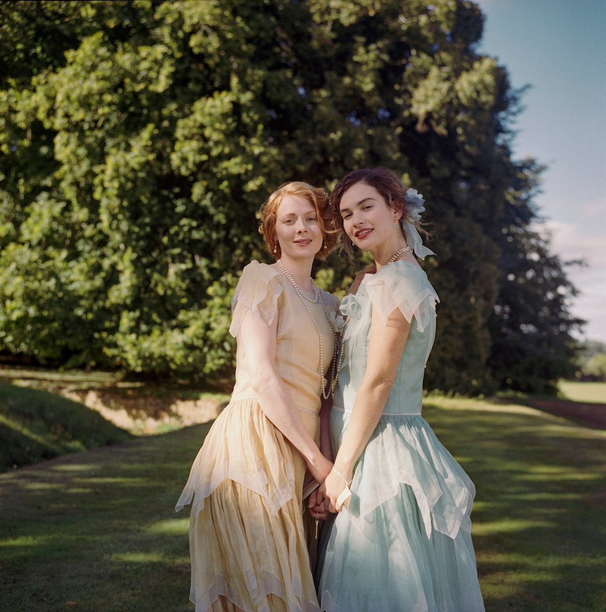 Emily Beecham as Fanny and Lily James as Linda, holding hands, in 'The Pursuit of Love'