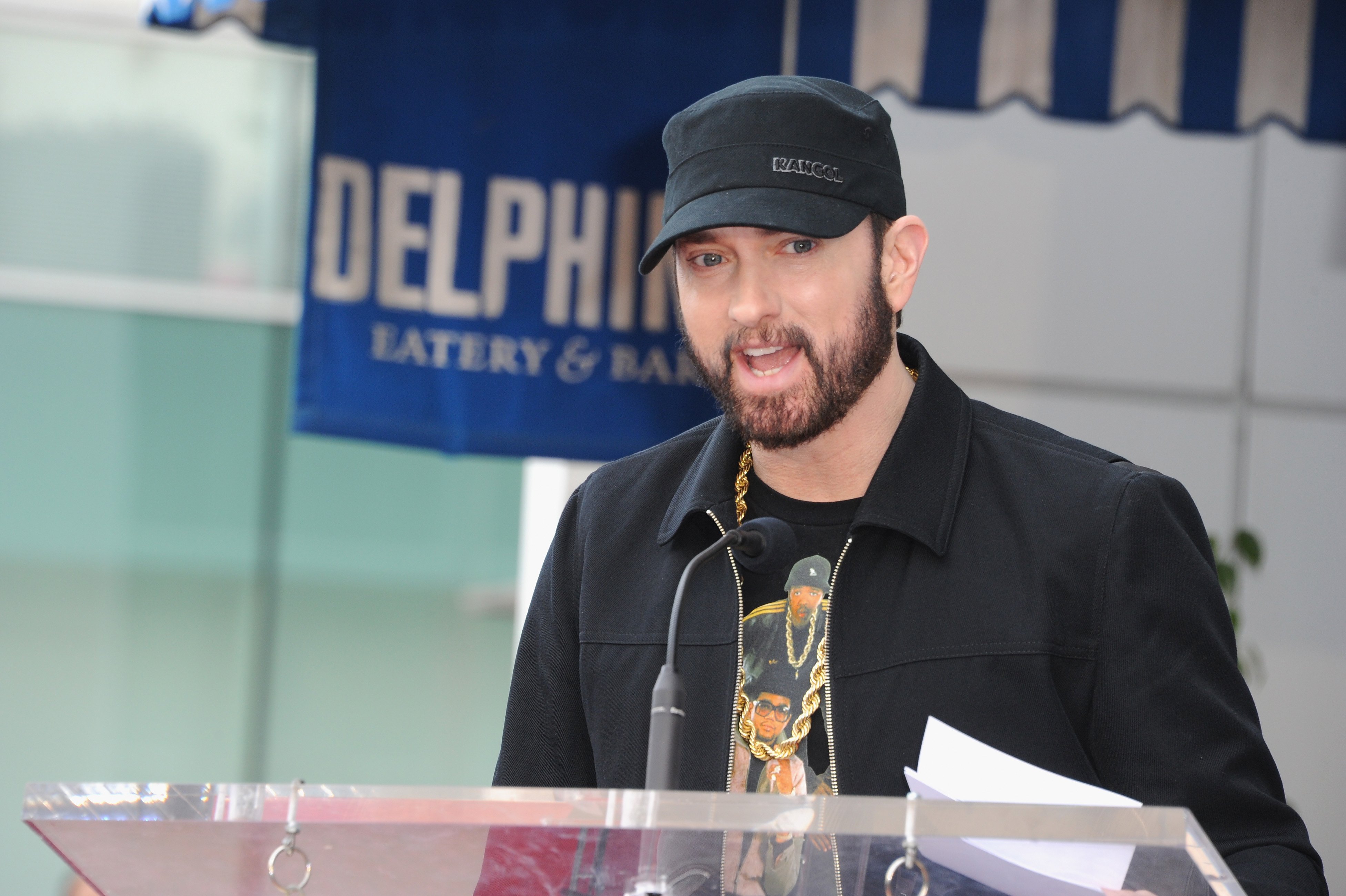 Eminem dressed in a black cap and jacket speaking at Curtis '50 Cent' Jackson's star ceremony on the Hollywood Walk of Fame