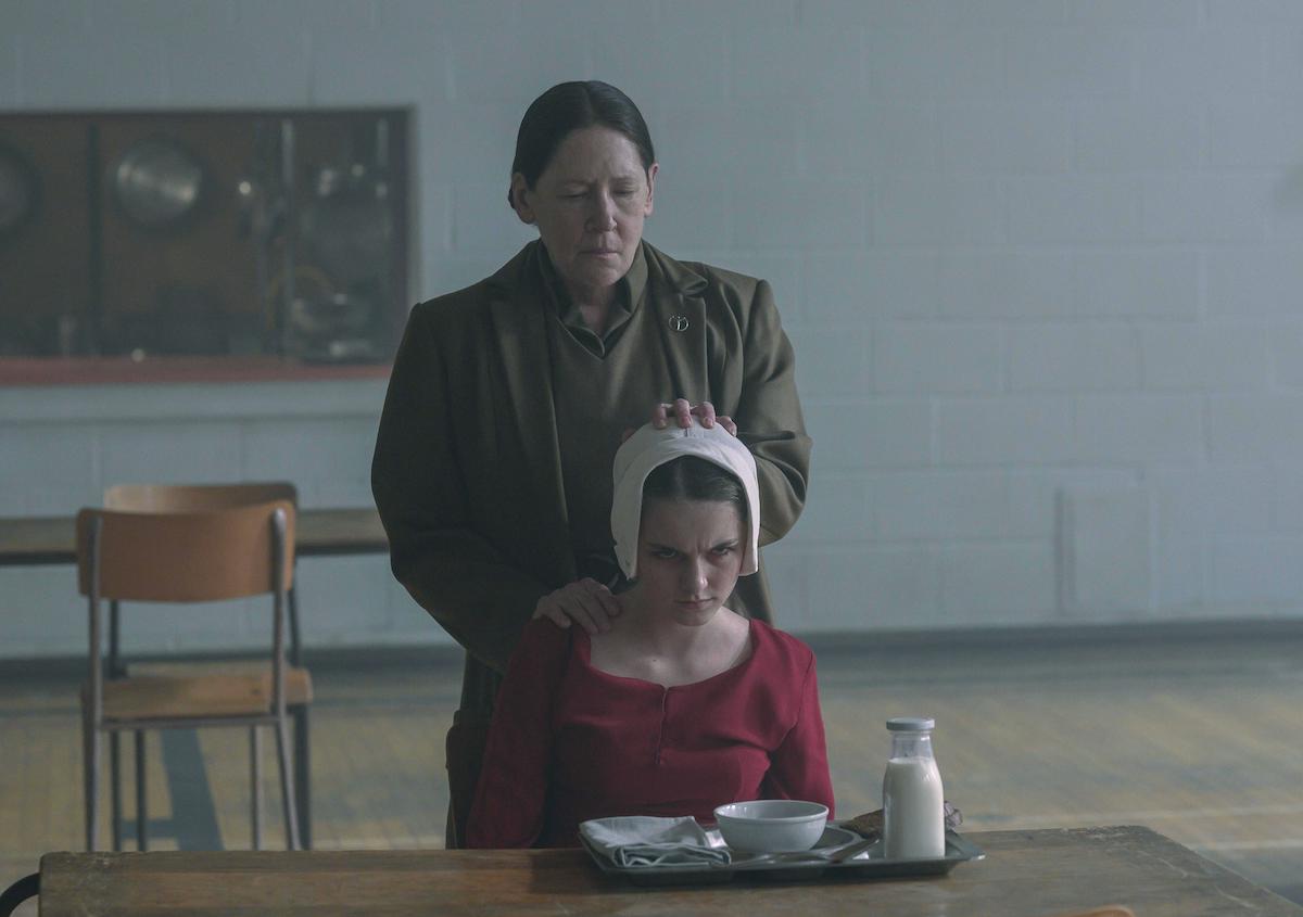 Ann Dowd as Aunt Lydia and Mckenna Grace as Esther Keyes in 'The Handmaid's Tale' Season 4. Dowd wears her brown Aunt uniform. Grace wears a red Handmaid dress and white bonnet.