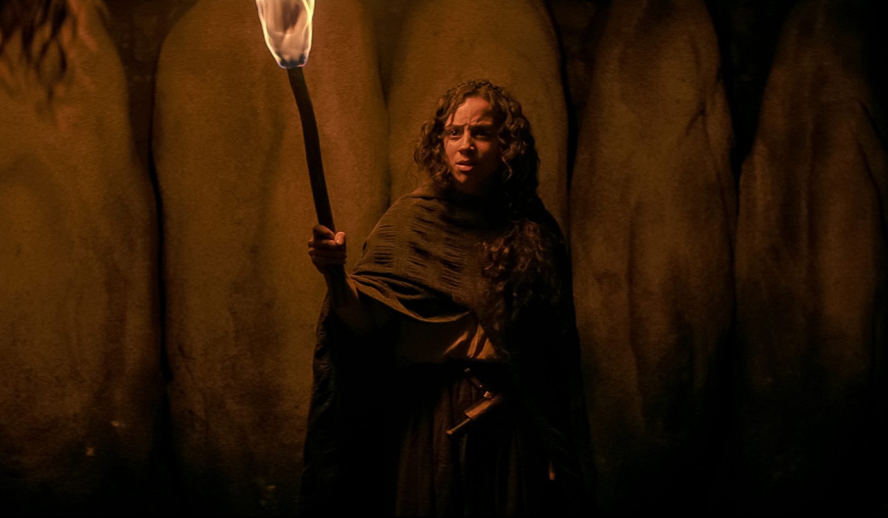 Kiana Madeira as Sarah Fier in the conclusion to Netflix's 'Fear Street' trilogy, 'Fear Street Part 3: 1666.' She's holding a torch and has a confused expression on her face.