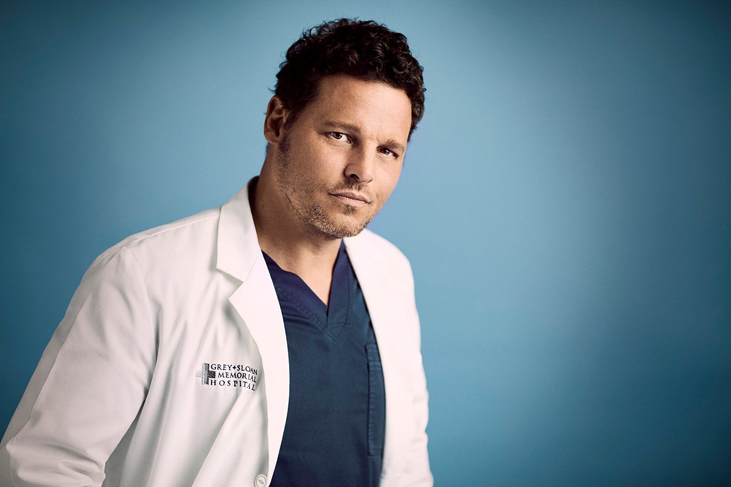 'Grey's Anatomy' actor Justin Chambers as Alex Karev wearing blue scrubs and smirking at the camera.