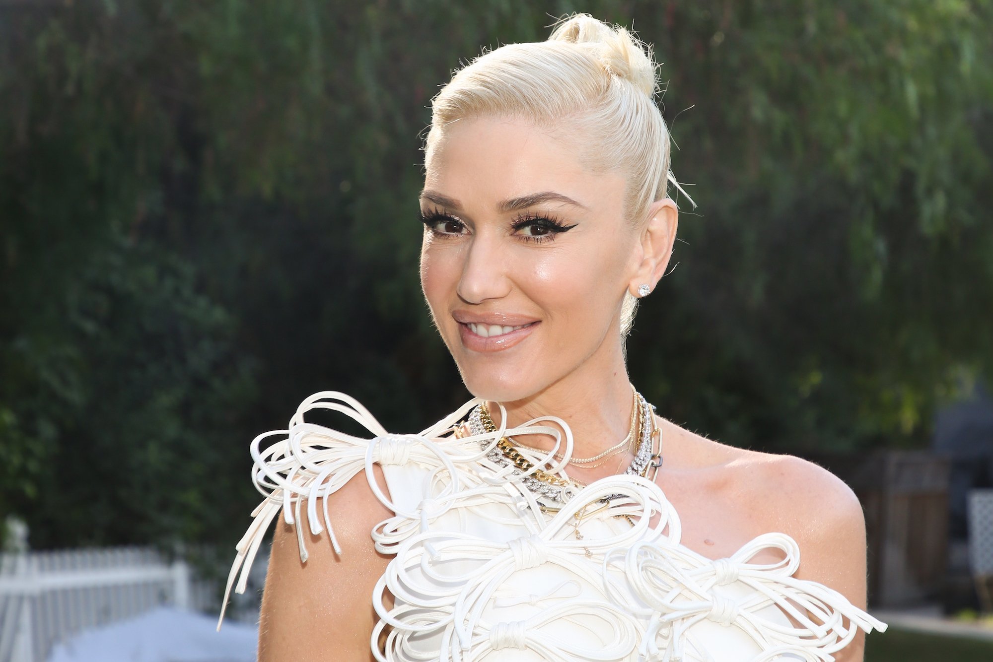Gwen Stefani smiling in front of a grove of bushes