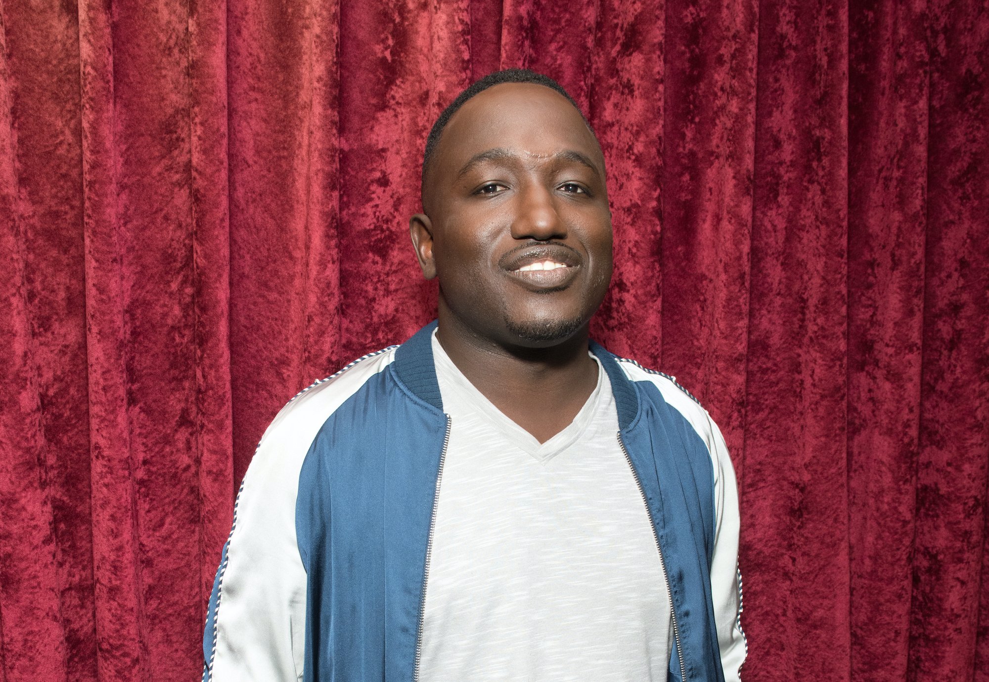 Hannibal Buress smiling in front of a red curtain