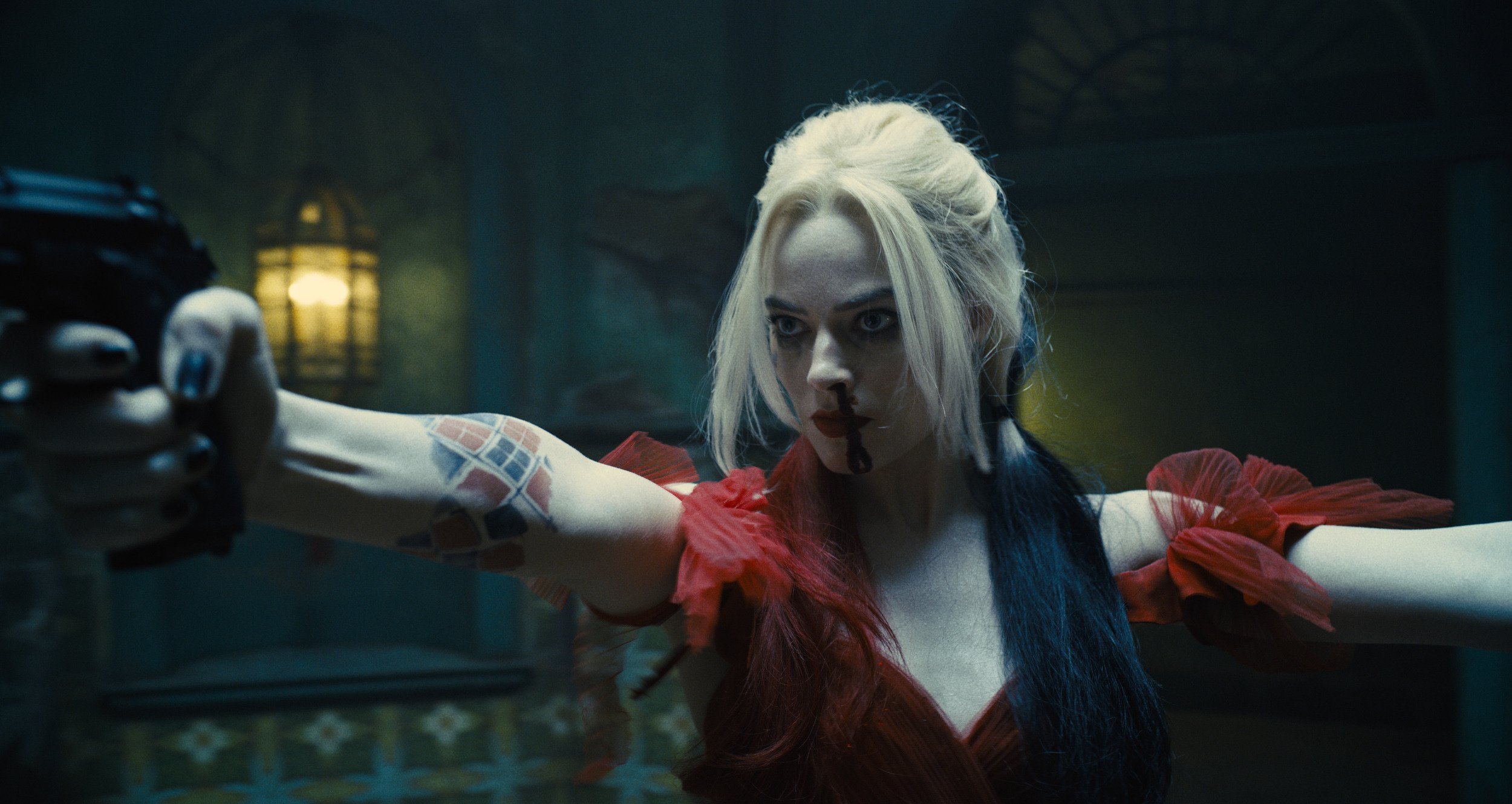 Margot Robbie as Harley Quinn in 'The Suicide Squad'. Her nose is bleeding and she's holding up two guns.