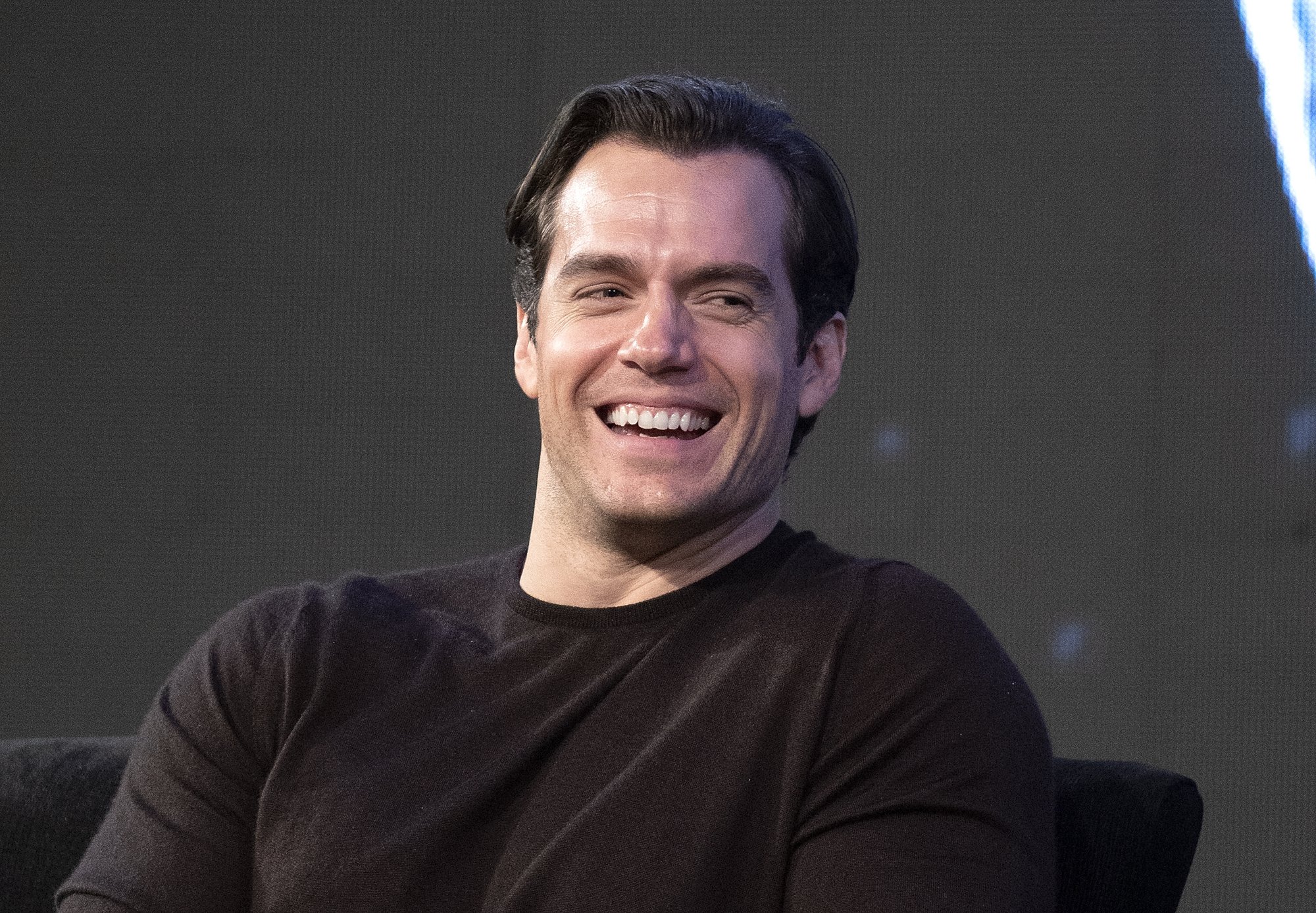 Henry Cavill, who was Stephenie Meyer's first pick for the lead role in Twilight, wearing a brown shirt and laughing