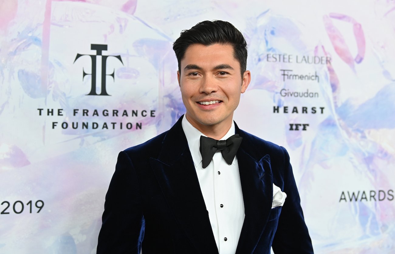 Henry Golding wearing a tuxedo in front of colorful background