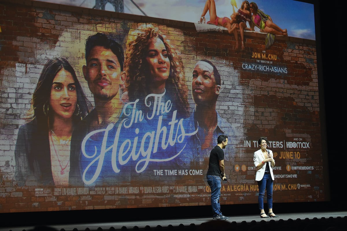 Lin-Manuel Miranda and Quiara Alegria Hudes speak onstage in front of a giant image of the ‘In the Heights’ poster