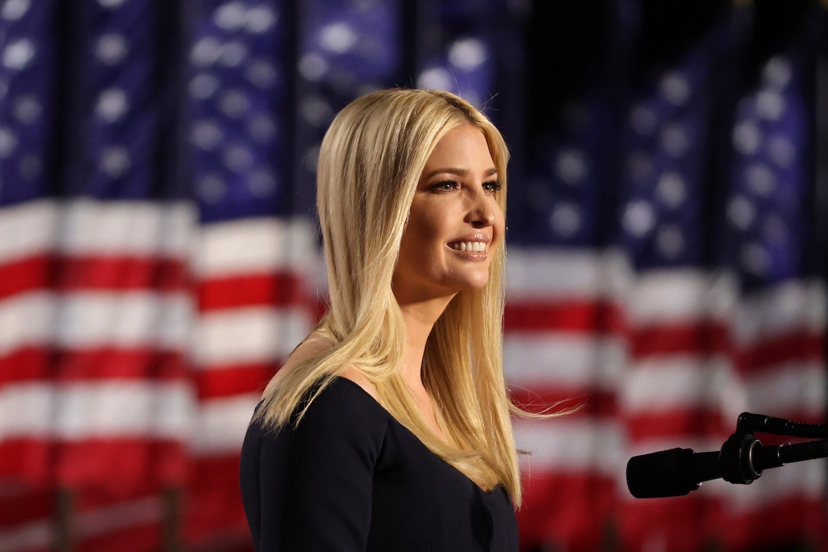 Ivanka Trump stands on stage smiling in front of an American flag.