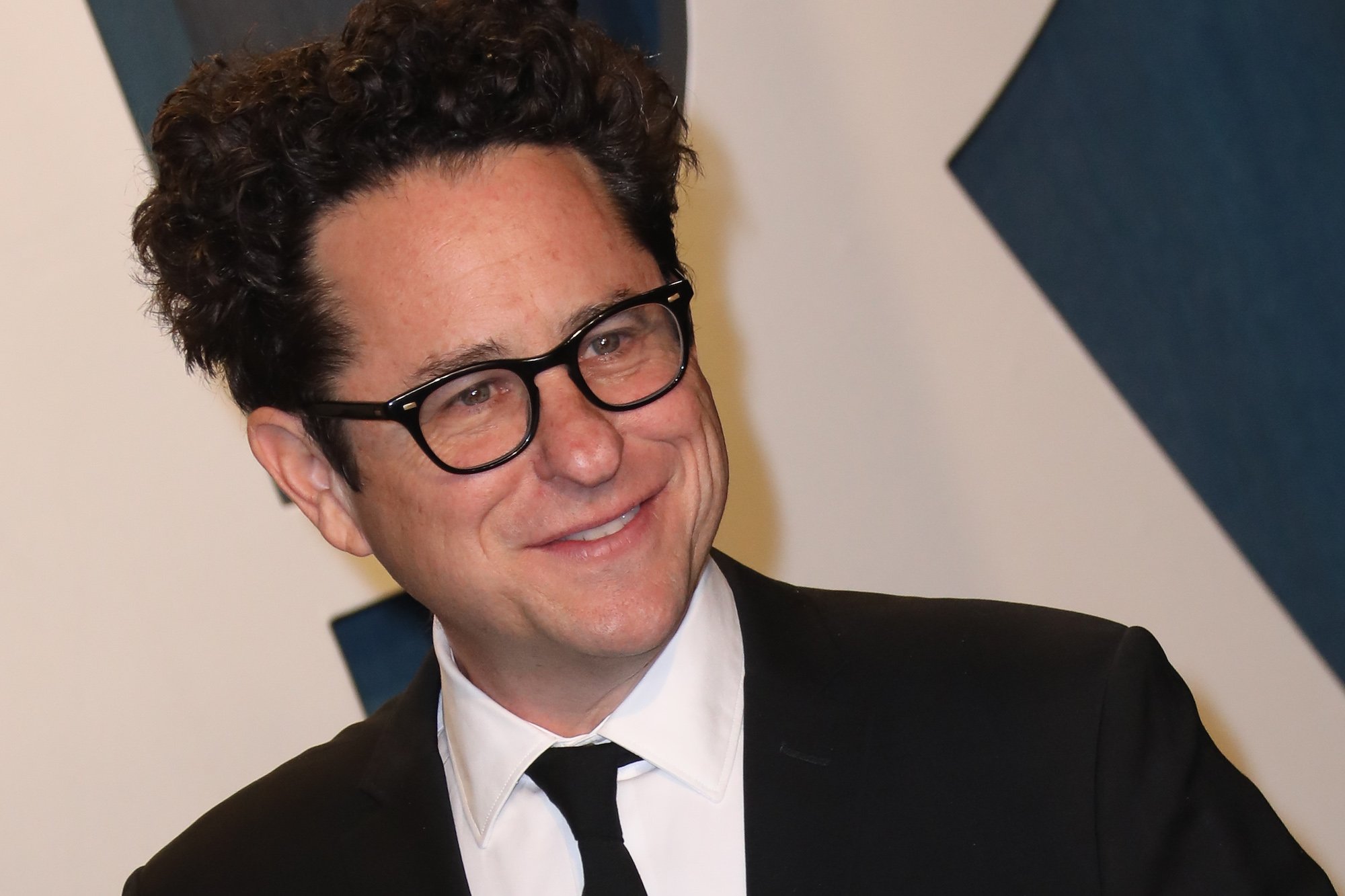 J.J. Abrams smiling in front of a white and blue background