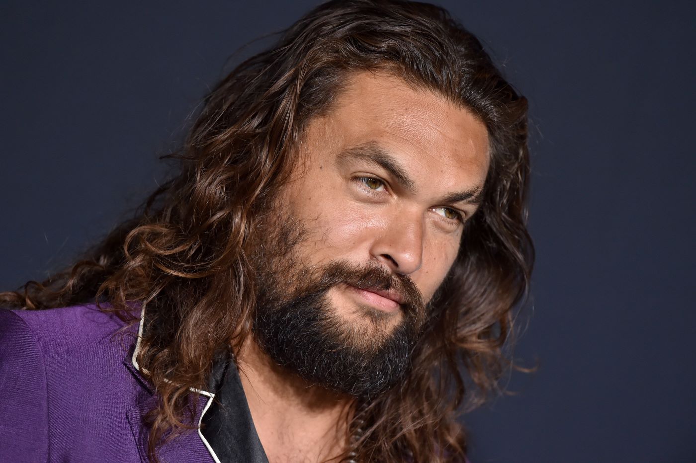 A closeup of Jason Momoa wearing a purple jacket with a black lapel.