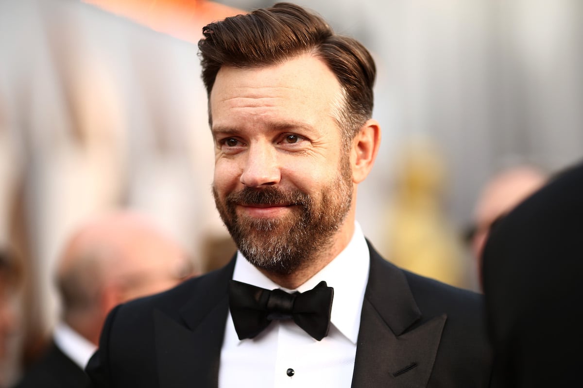 Jason Sudeikis smiles on a red carpet in a black suit and bow tie.