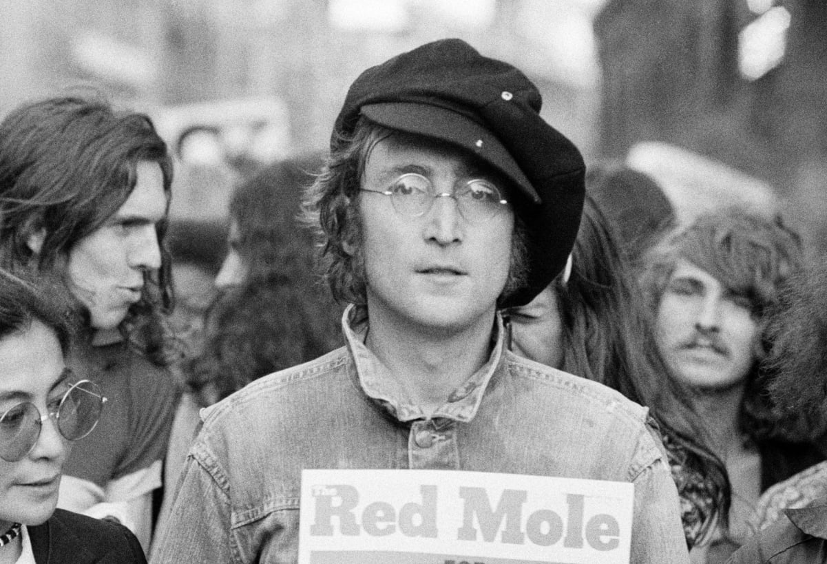 John Lennon wears a black cap, denim jacket, and his famed spectacles in a photograph from 1975.