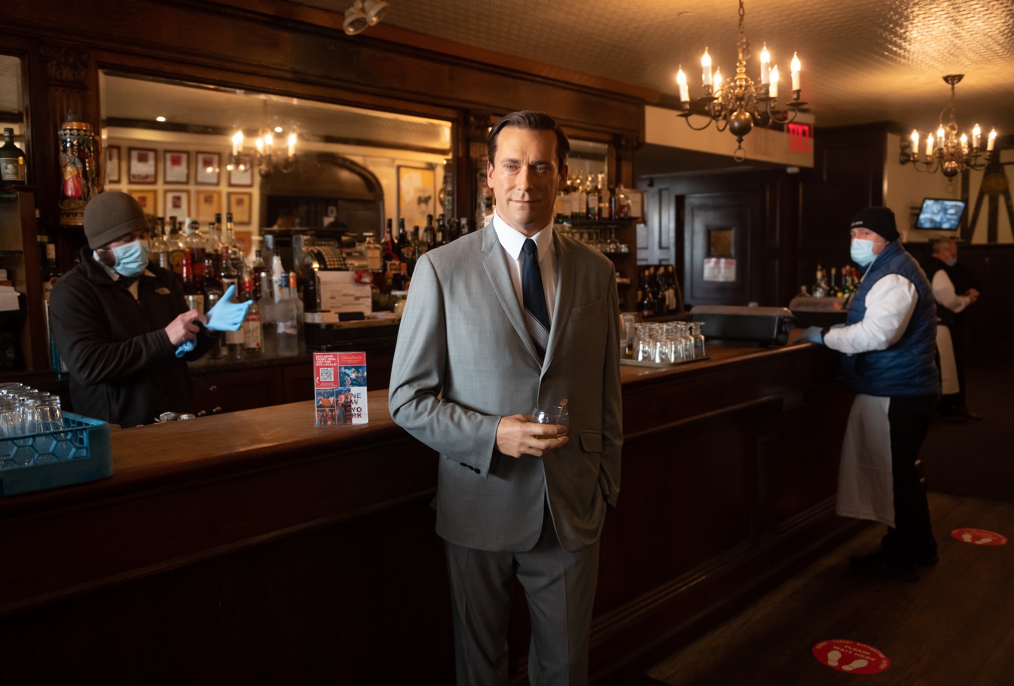 Madame Tussauds' Jon Hamm wax figure holds a glass of whiskey by the bar at Peter Luger Steak House in New York City in February 2021