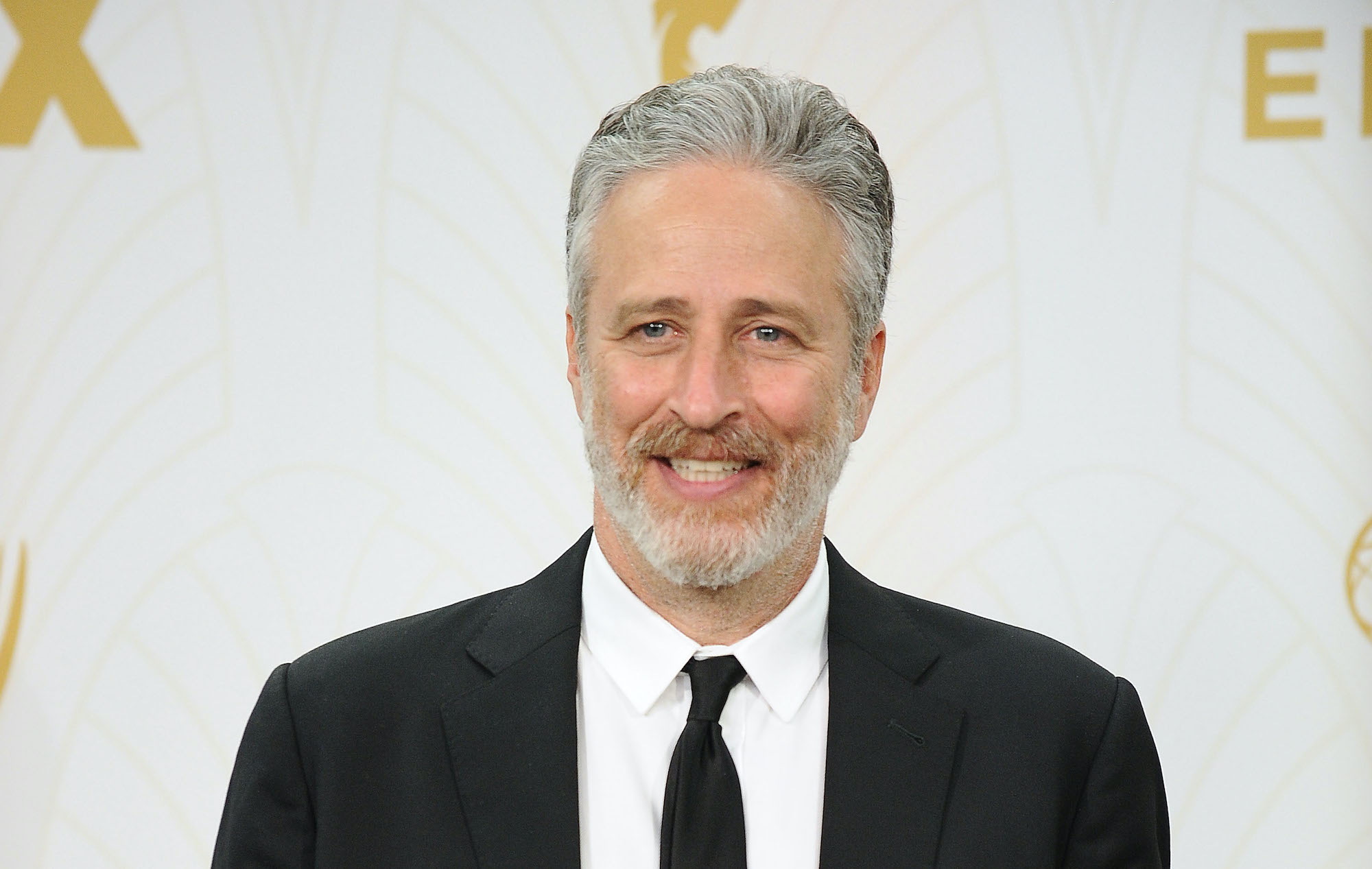 Jon Stewart smiling in front of a white background