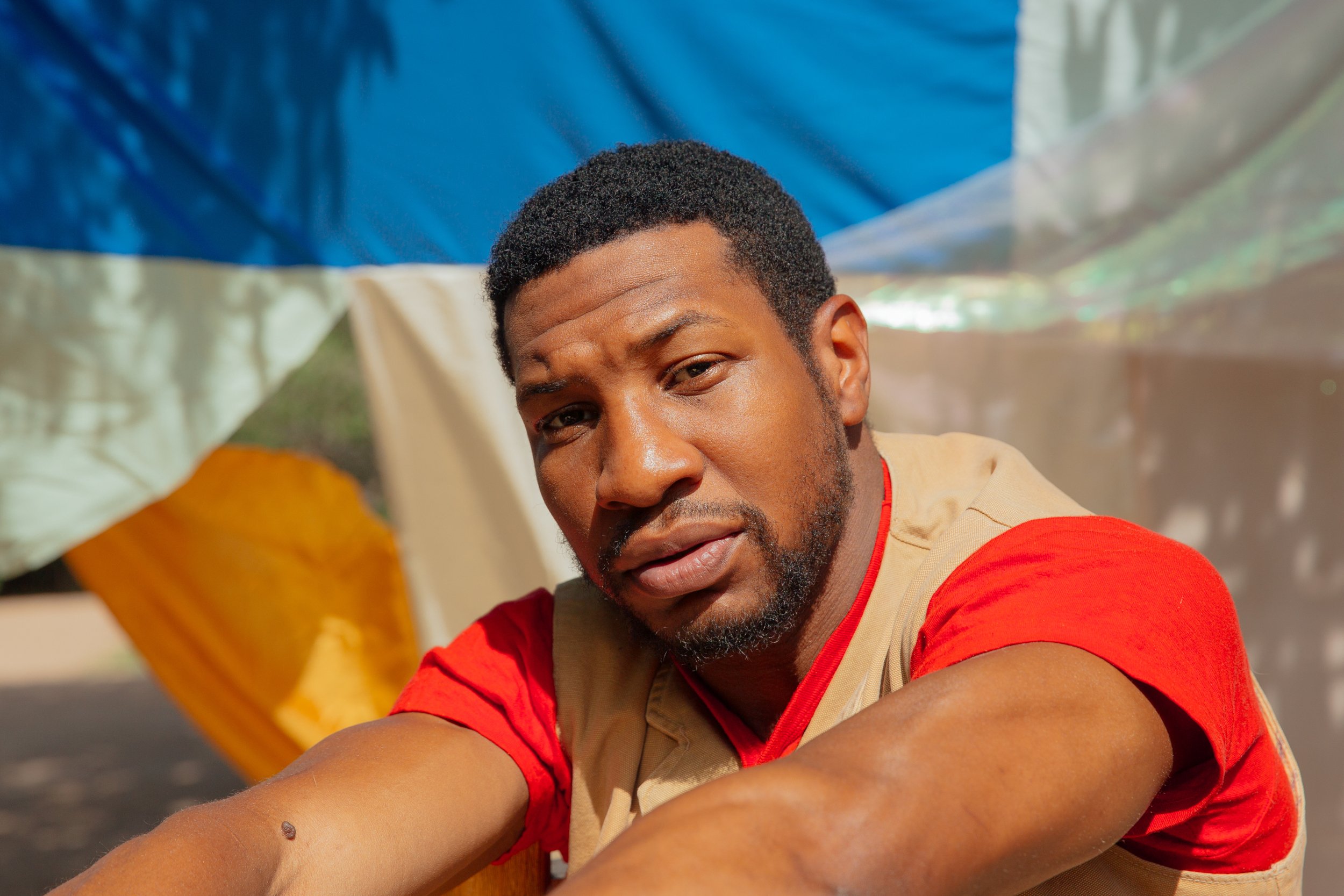 Jonathan Majors wearing a red and biege shirt and smiling