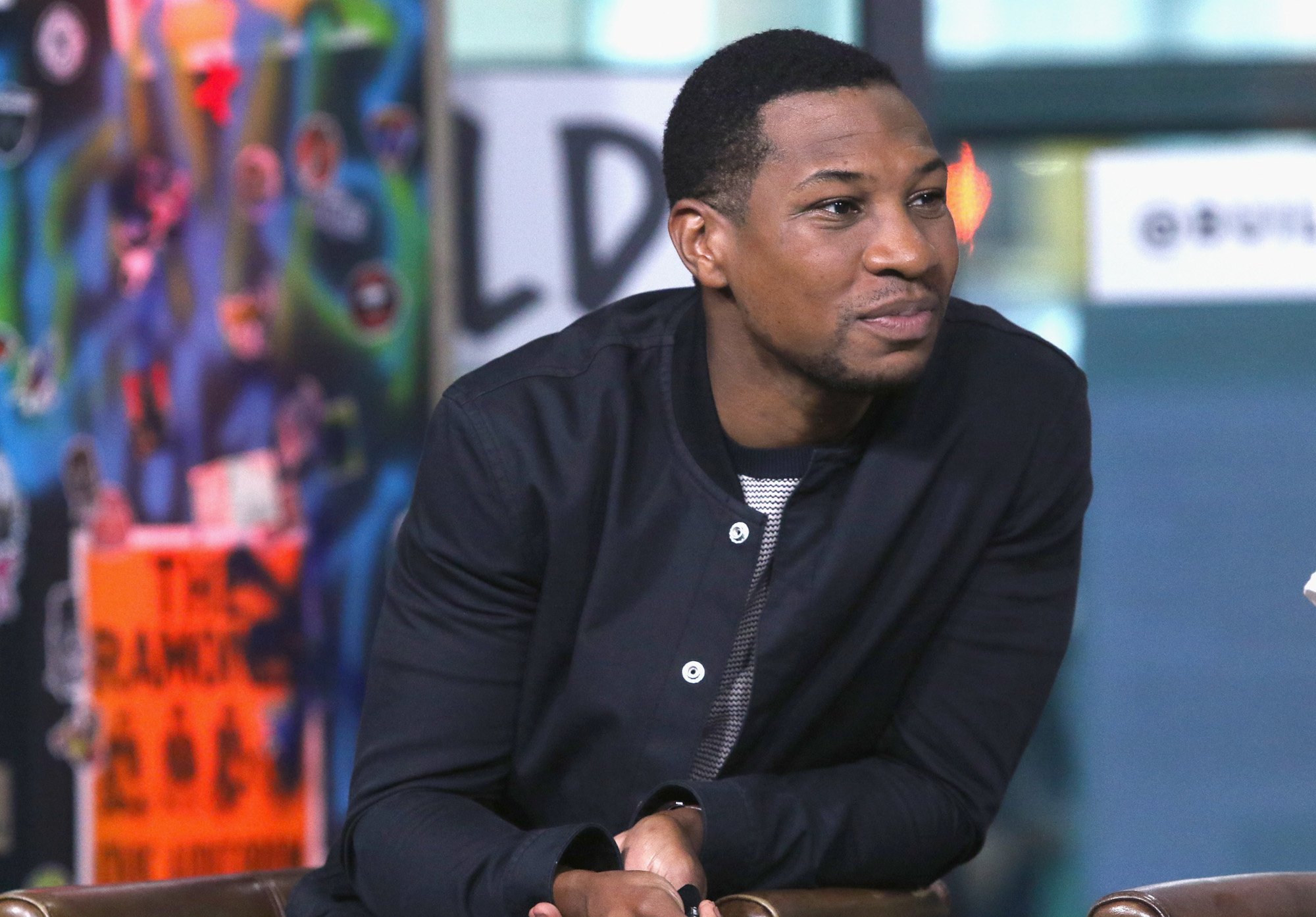 Jonathan Majors wearing a black shirt and leaning over during an event