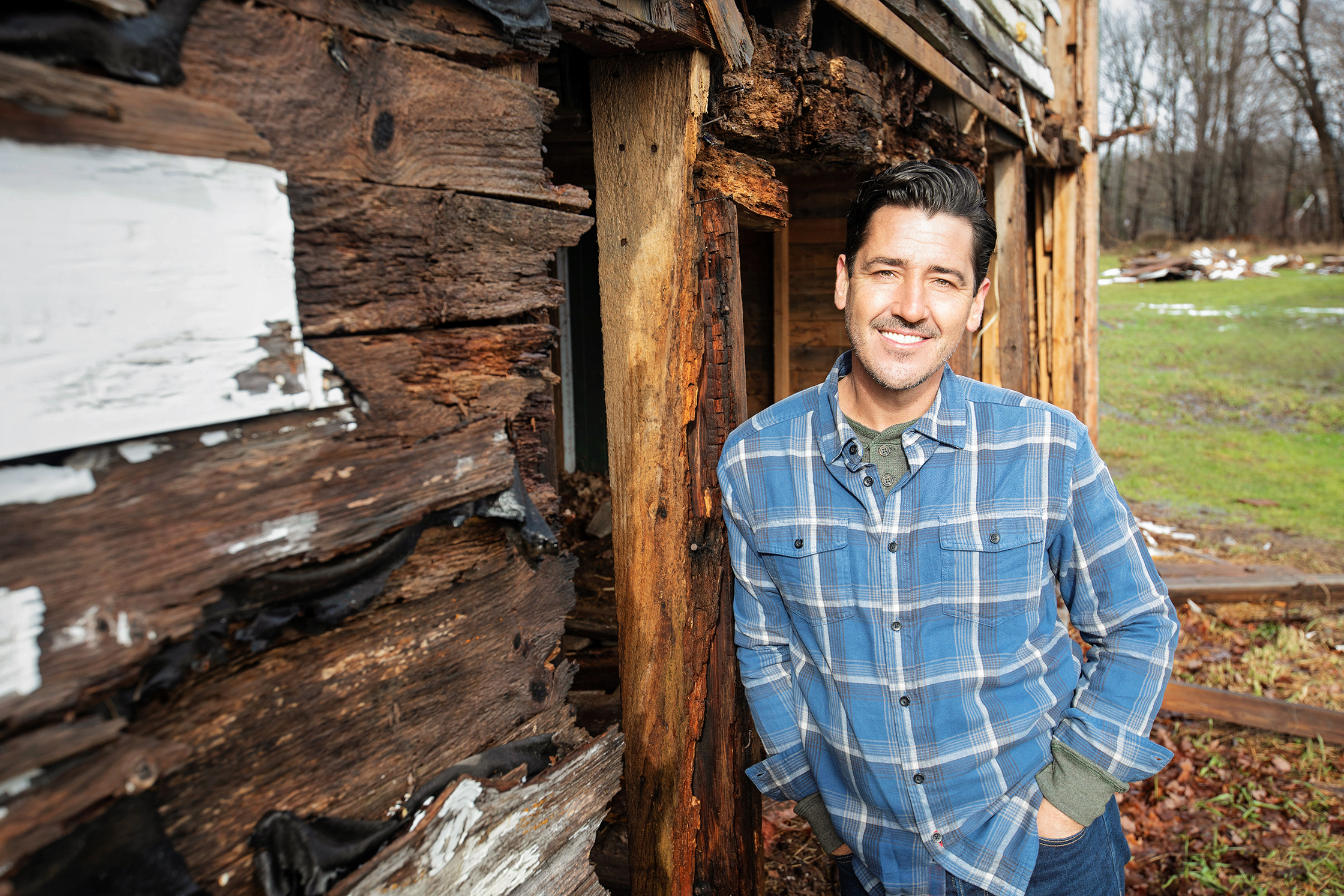 Jonathan Knight wearing a blue shirt and standing in front of a log house