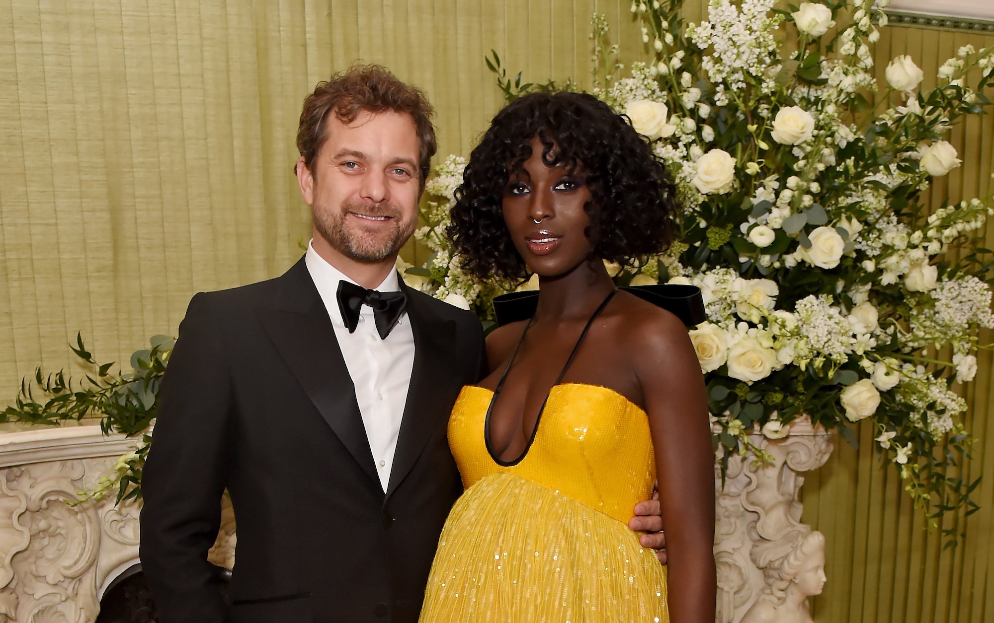 Joshua Jackson and wife Jodie Turner-Smith smiling in front of a white floral arrangement