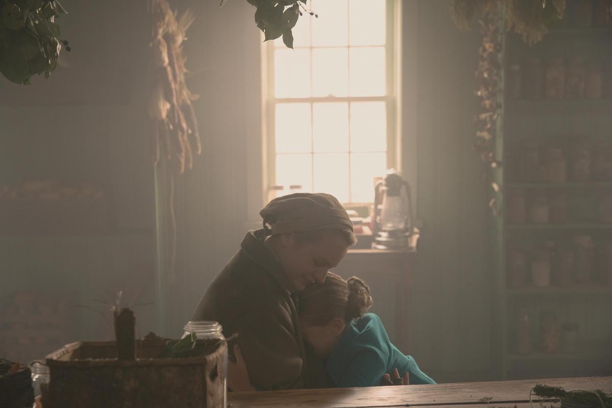 Elisabeth Moss as June and Mckenna Grace as Esther in 'The Handmaid's Tale' Season 4. June wears a beige Martha uniform as she hugs Esther, who wears a teal Wife dress.