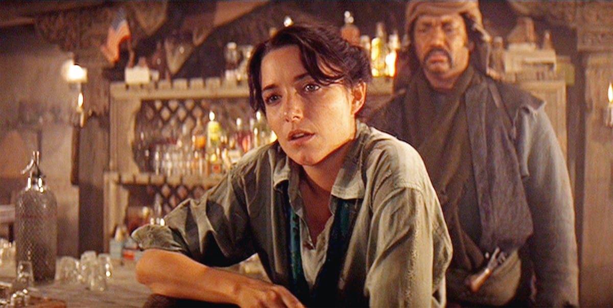 Karen Allen as Marion Ravenwood sitting in a bar with a fire behind her in 'Indiana Jones and the Raiders of the Lost Ark'