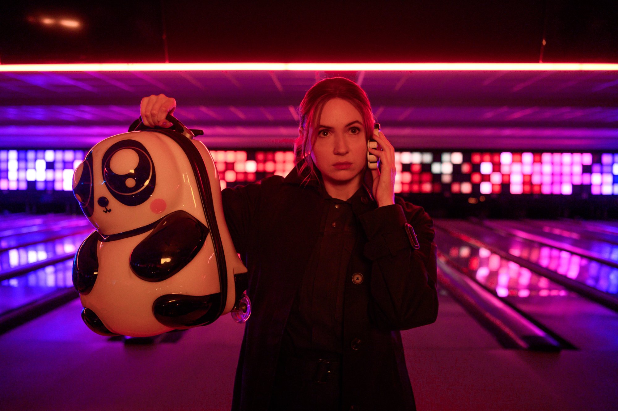 Karen Gillan as Sam in Gunpowder Milkshake. She's holding up a backpack and standing in a bowling alley.