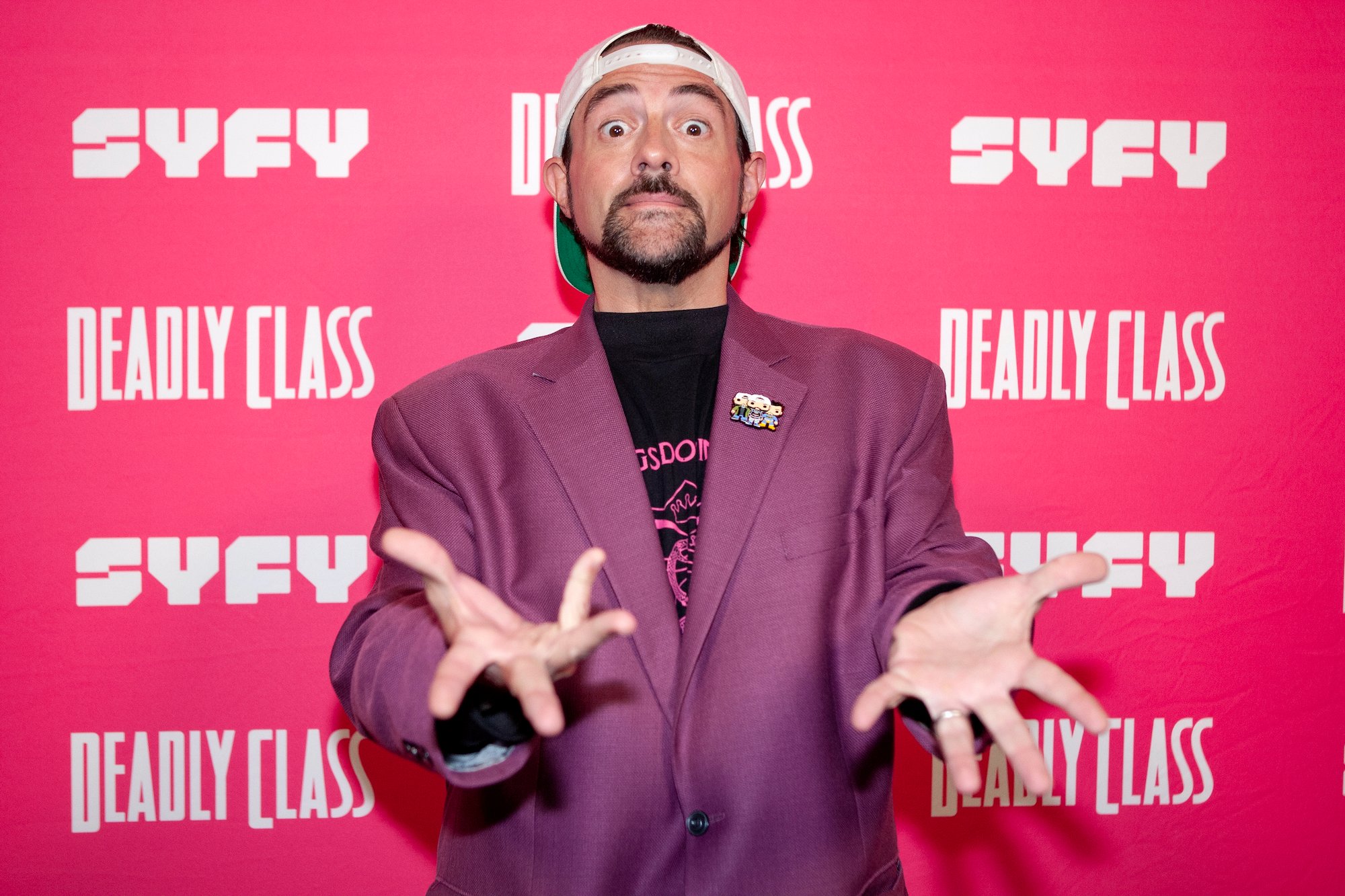 Kevin Smith holding his hands out, standing in front of a pink background