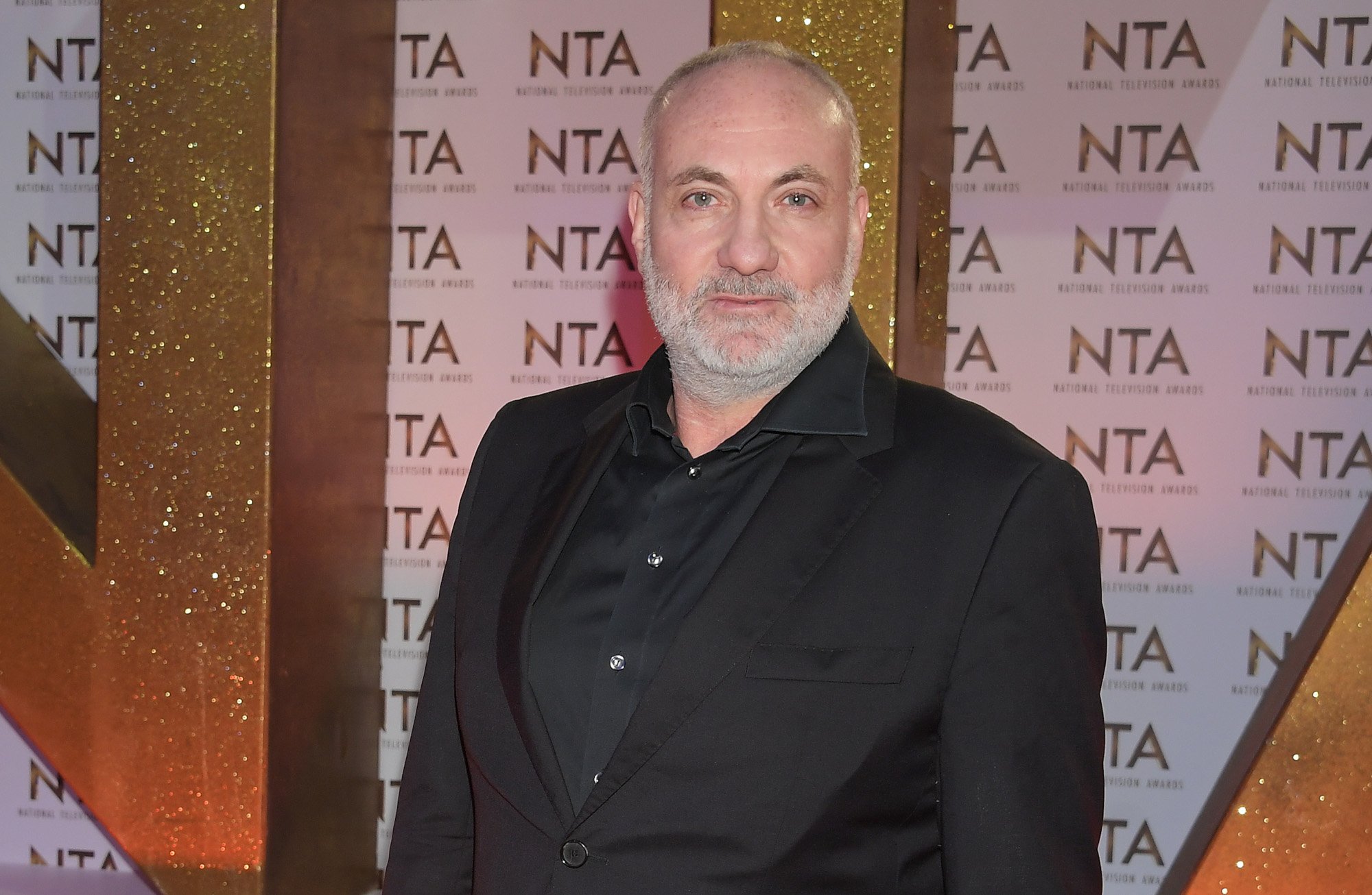 Kim Bodnia wearing a black suit and standing in front of a National Television Awards wall
