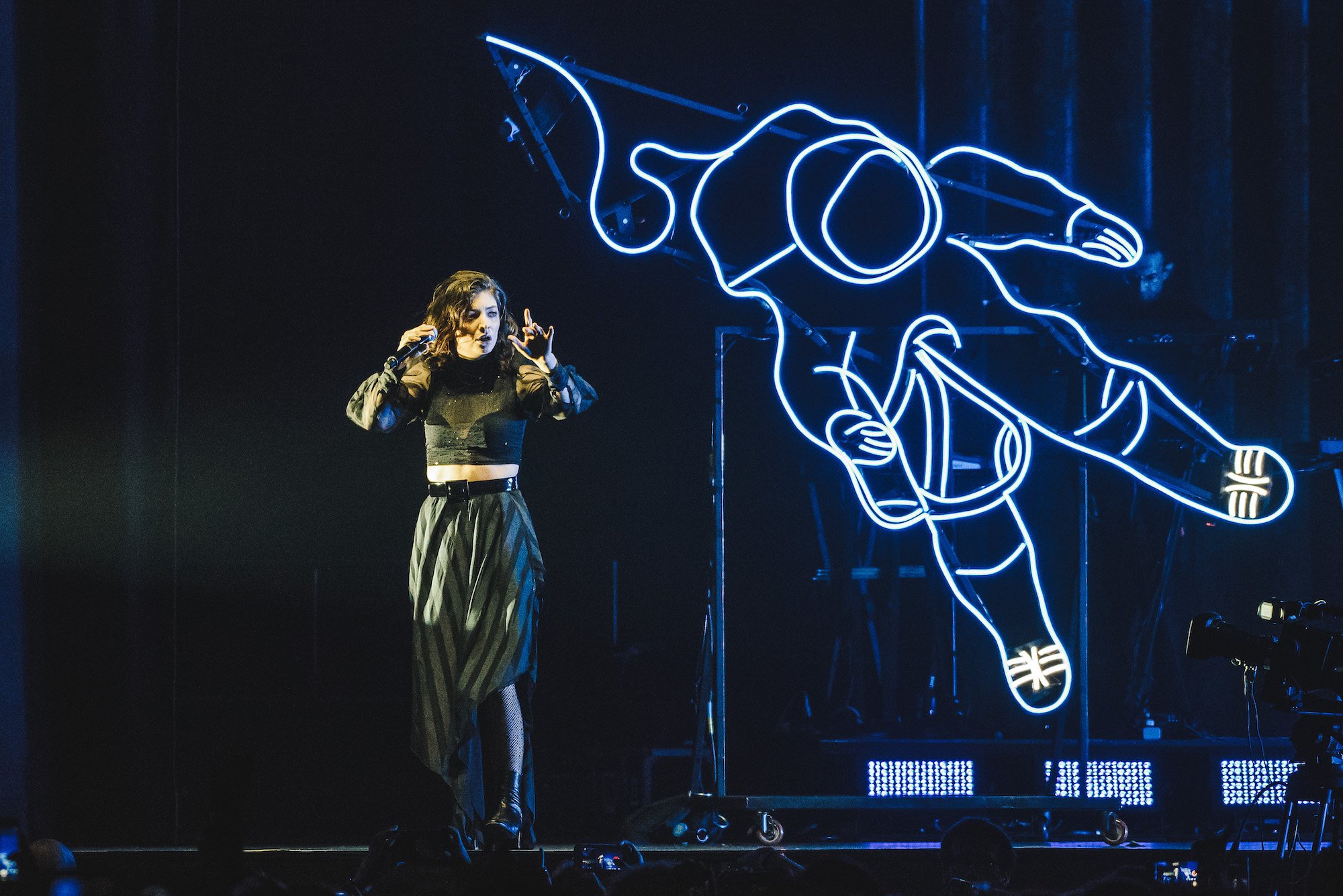 Lorde performing on stage in front of a neon hand-shaped light sculpture