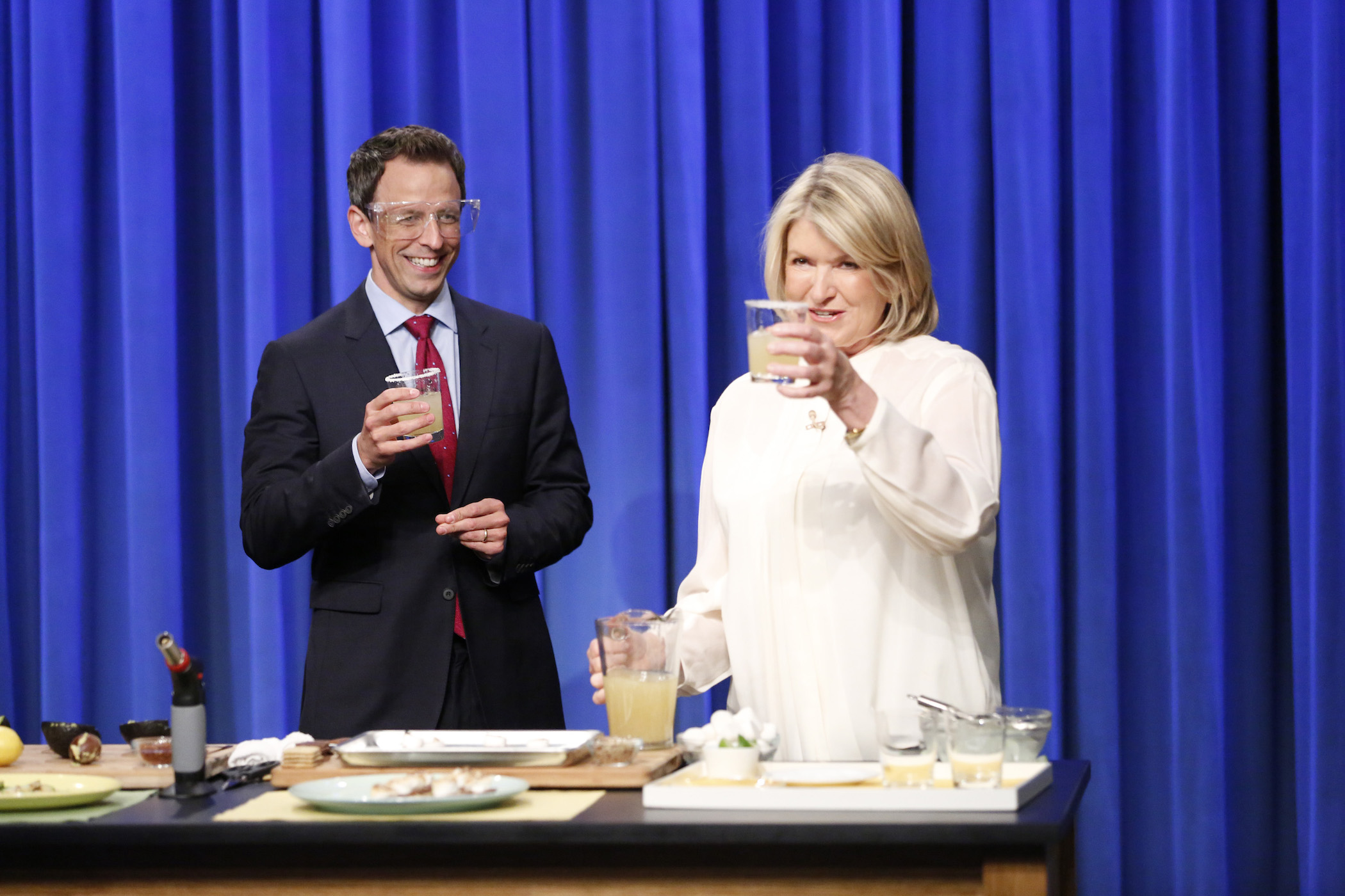 Seth Meyers and Martha Stewart holding up cocktails after making one of Martha Stewart's recipes on TV