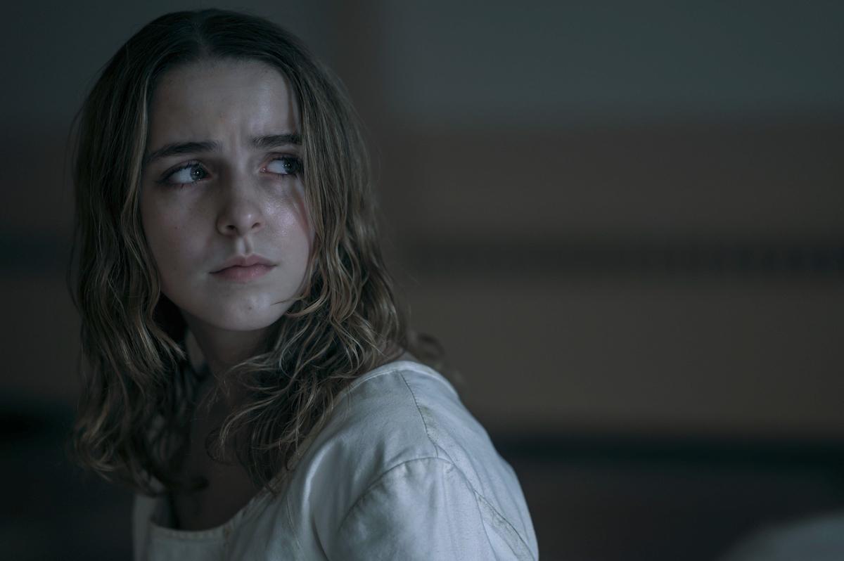 Mckenna Grace as Esther Keyes in 'The Handmaid's Tale' Season 4. Her blonde hair is down and she wears a white nightgown.