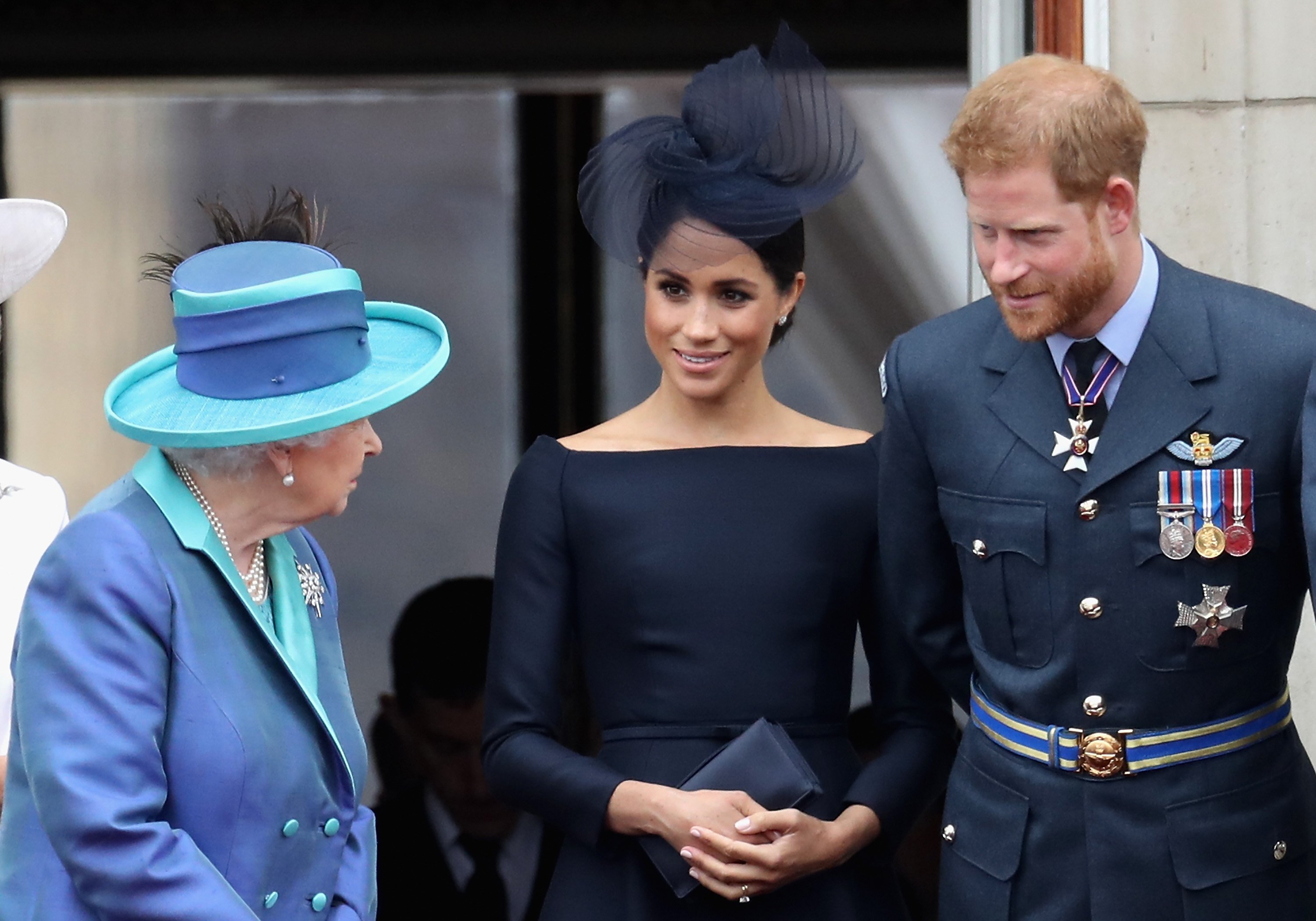 Meghan Markle and Prince Harry standing on the Buckingham Palace balcony with Queen Elizabeth II to watch the RAF flypast