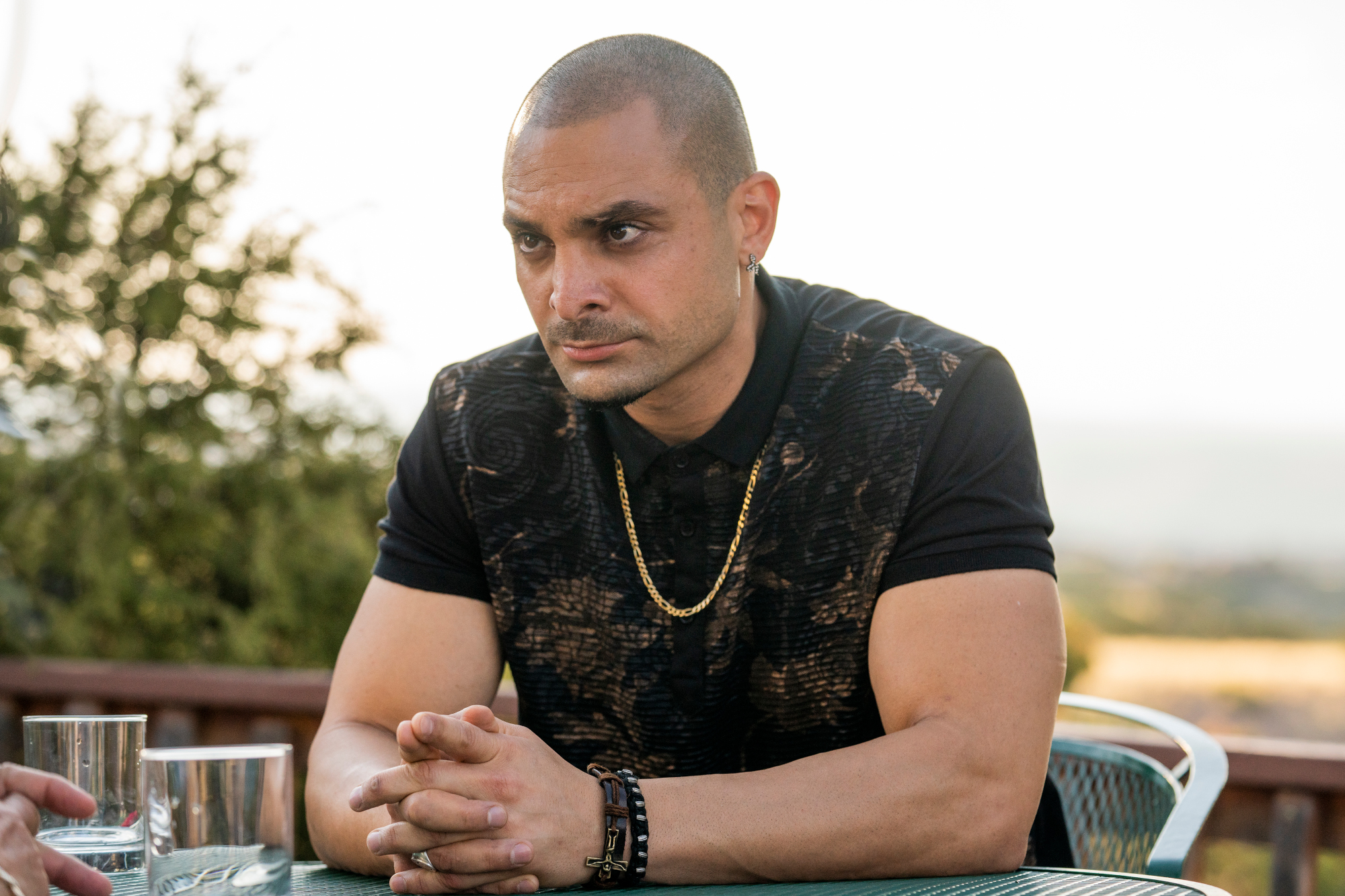Michael Mando as Nacho Varga in AMC's 'Better Call Saul' - He's sitting at a table and leaning over with his hands clasped together