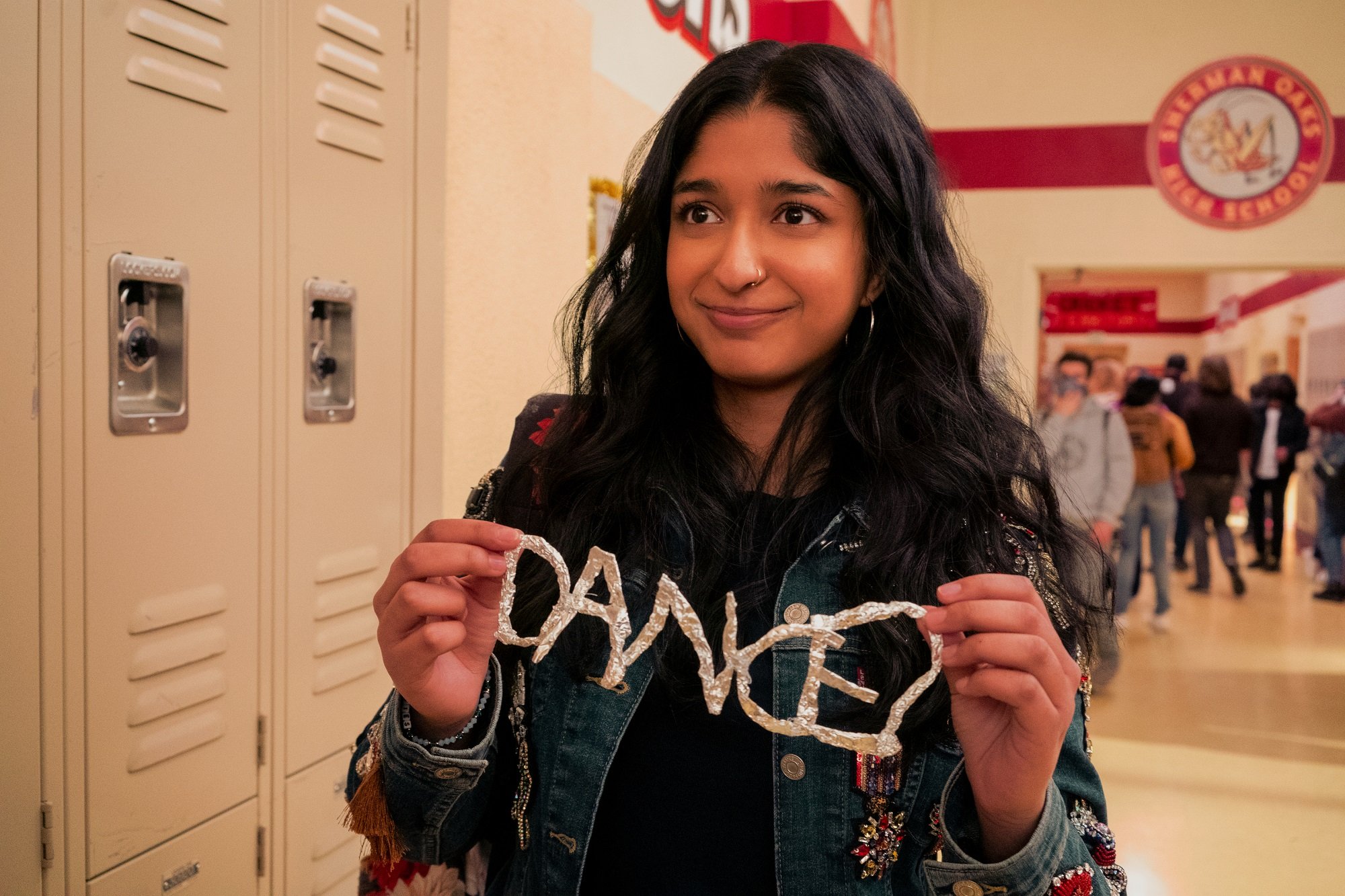 Devi holds up a homemade sign that spells 'Dance?' in 'Never Have I Ever'